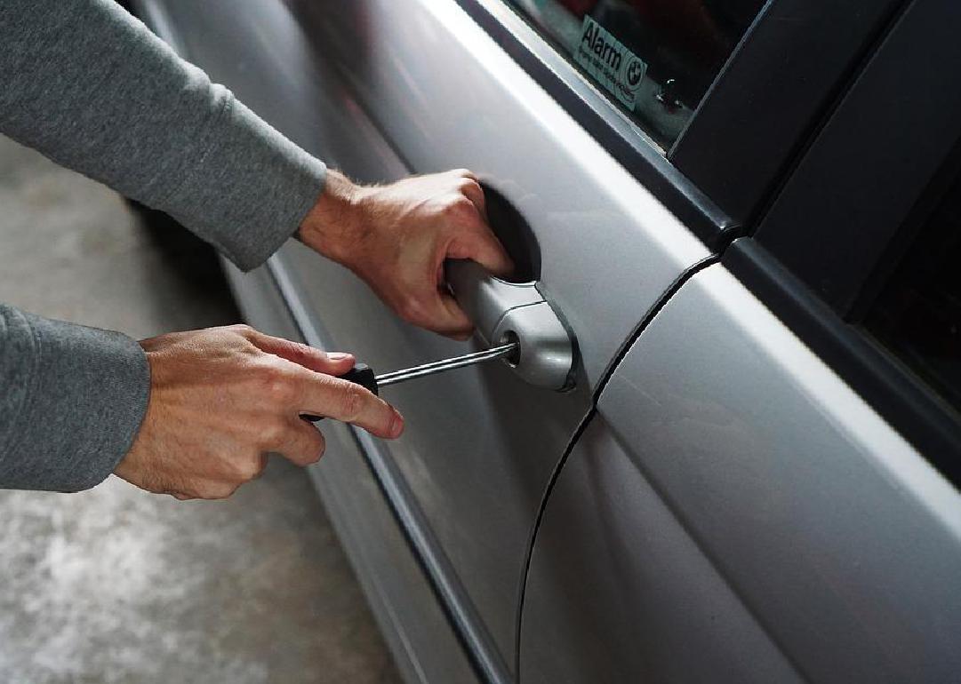 A close up on a pair of hands using a screwdriver to try to break into a car. 