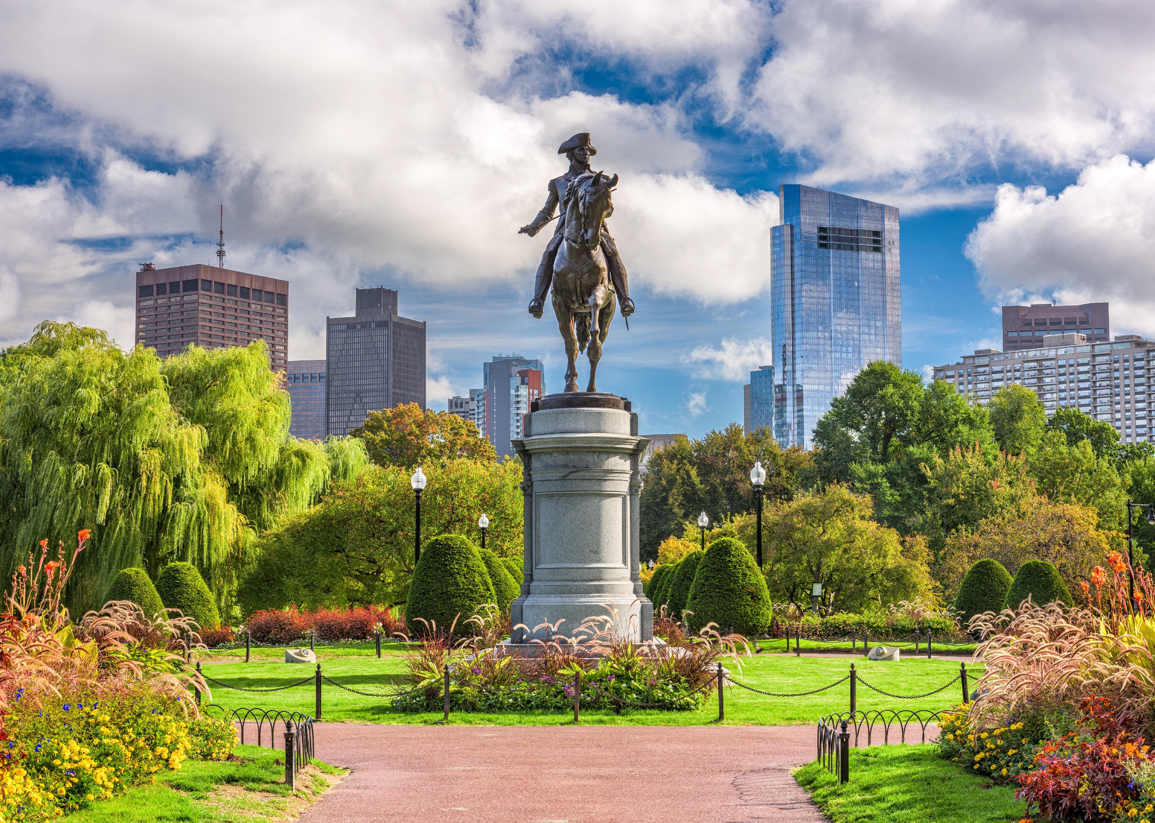 A statue of a man on a horse with the Boston skyline in the background.