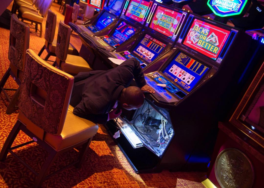 A security guard uses a flashlight to inspect the inside of a gambling machine.