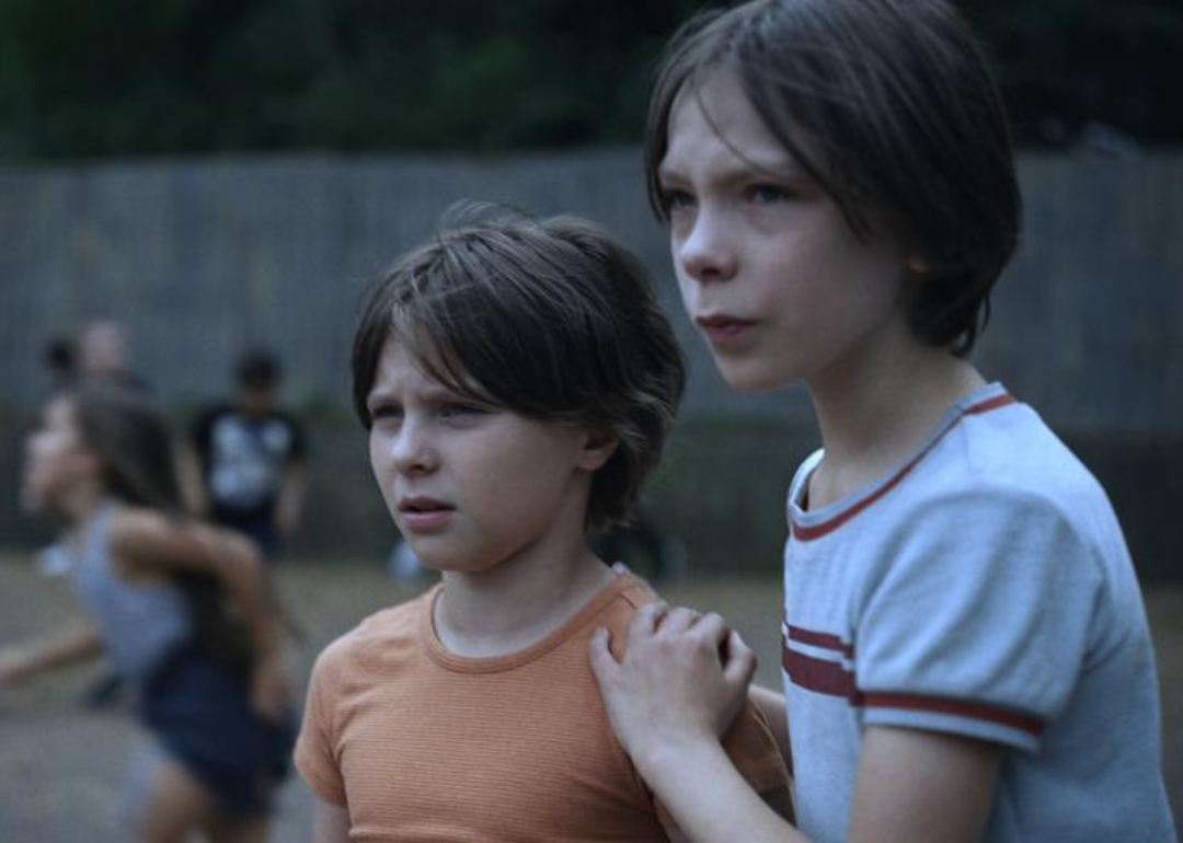 A worried-looking little girl holds onto a little boy on the playground.