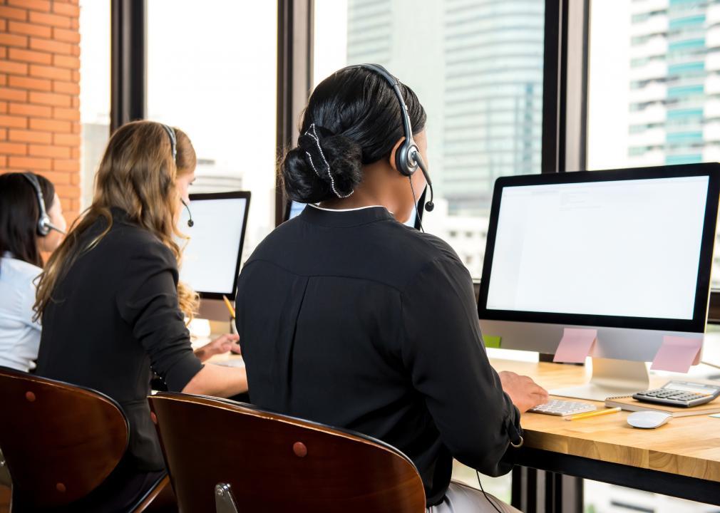 Three people wearing headsets sat in front of computer monitors in an office.