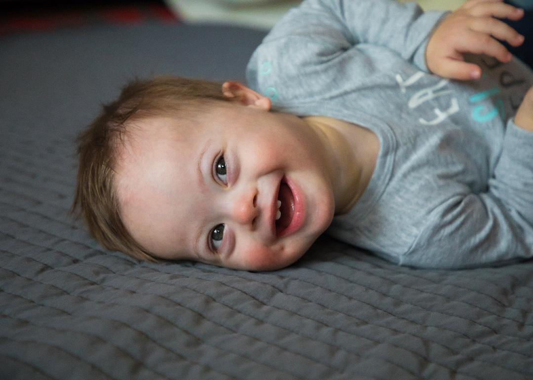 Smiling baby on gray bedding.