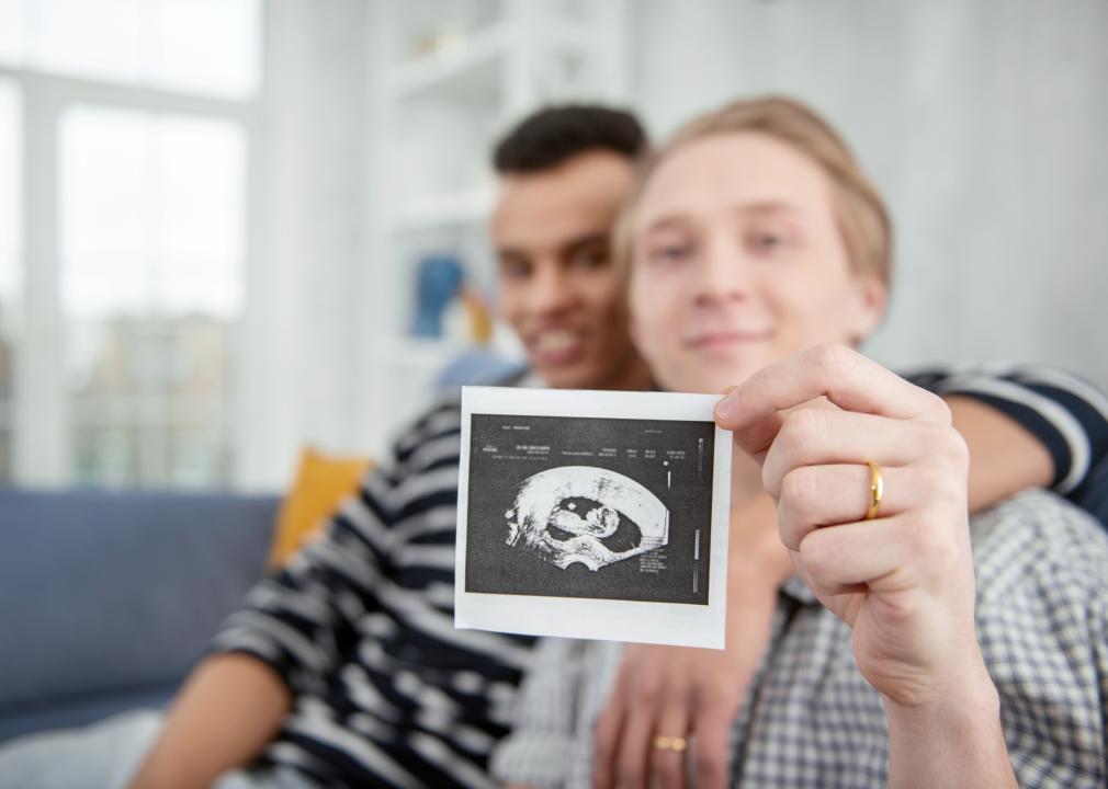Couple sitting on couch, one holding a ultrasound picture