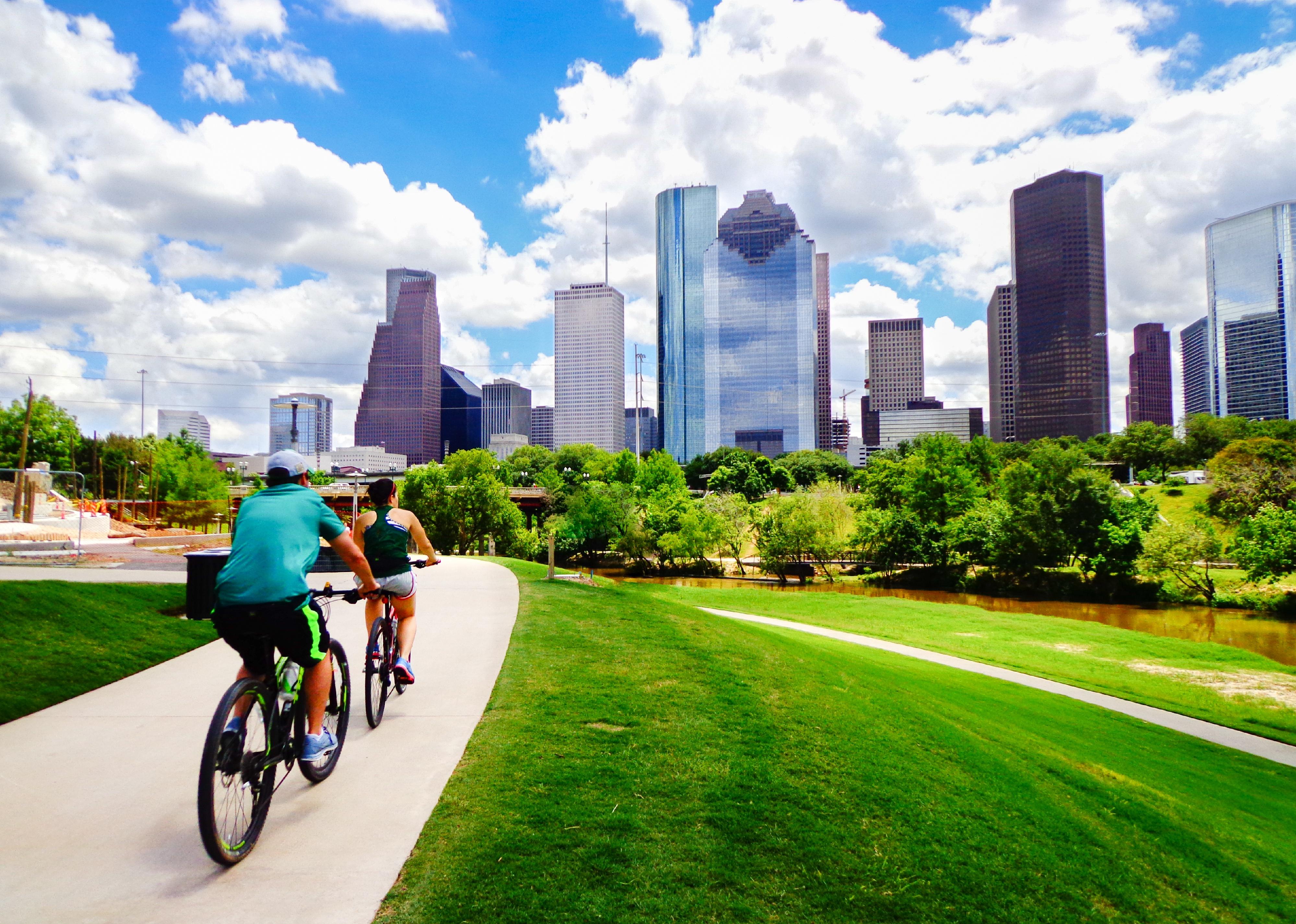 Two people riding bikes toward high rise buildings