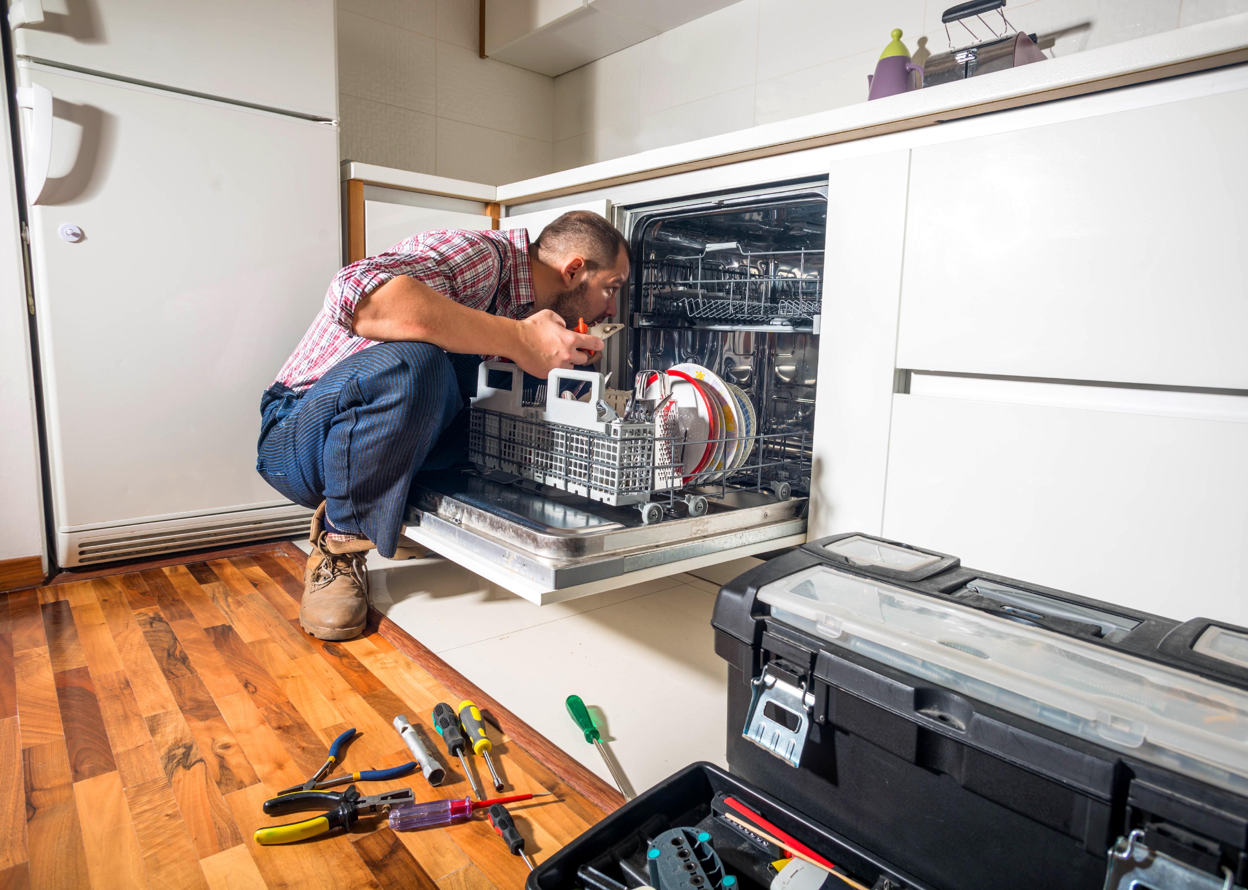 Person repairs dishwasher in a kitchen.