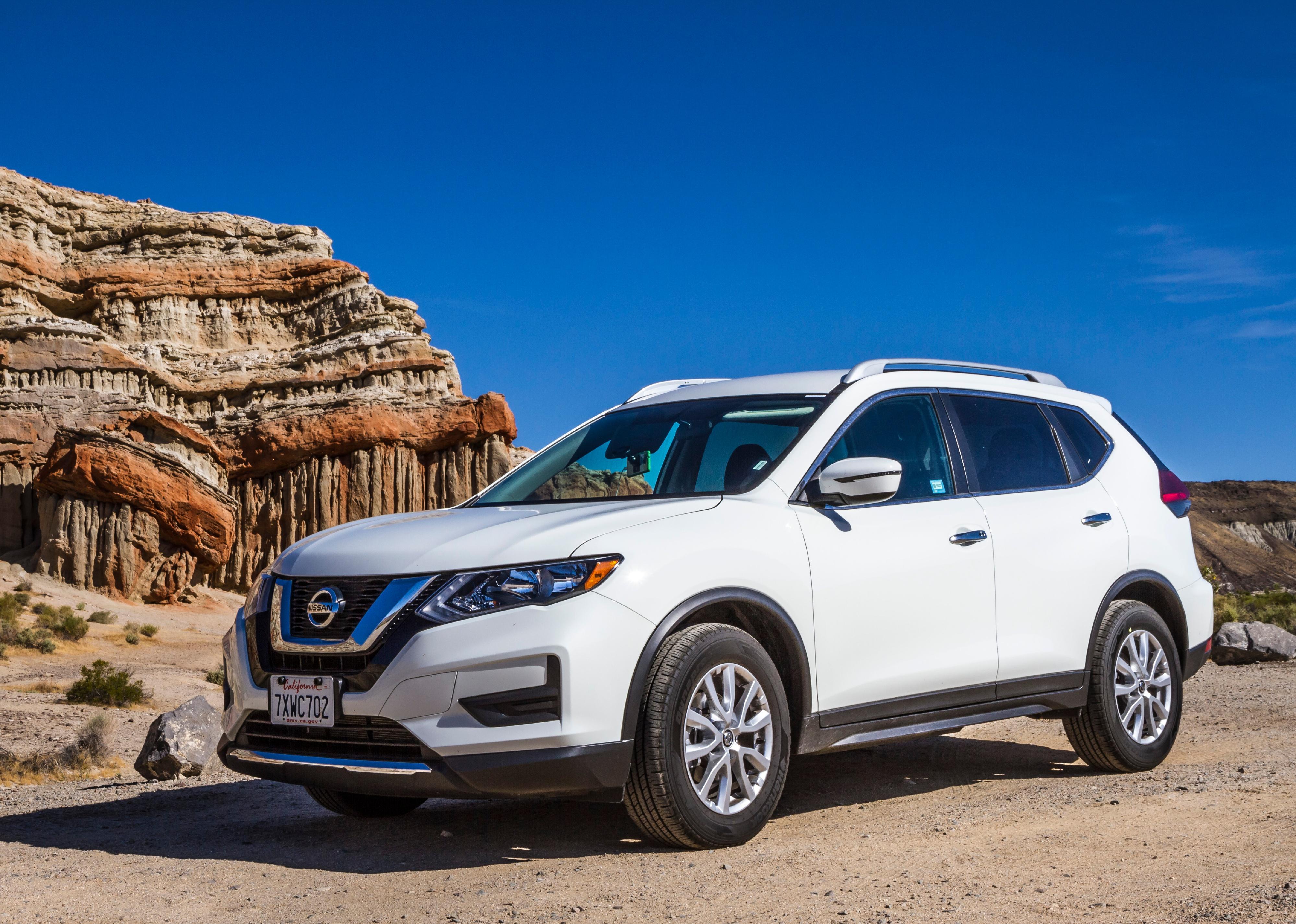 White Nissan Rogue on gravel road in front of sandstone formation.