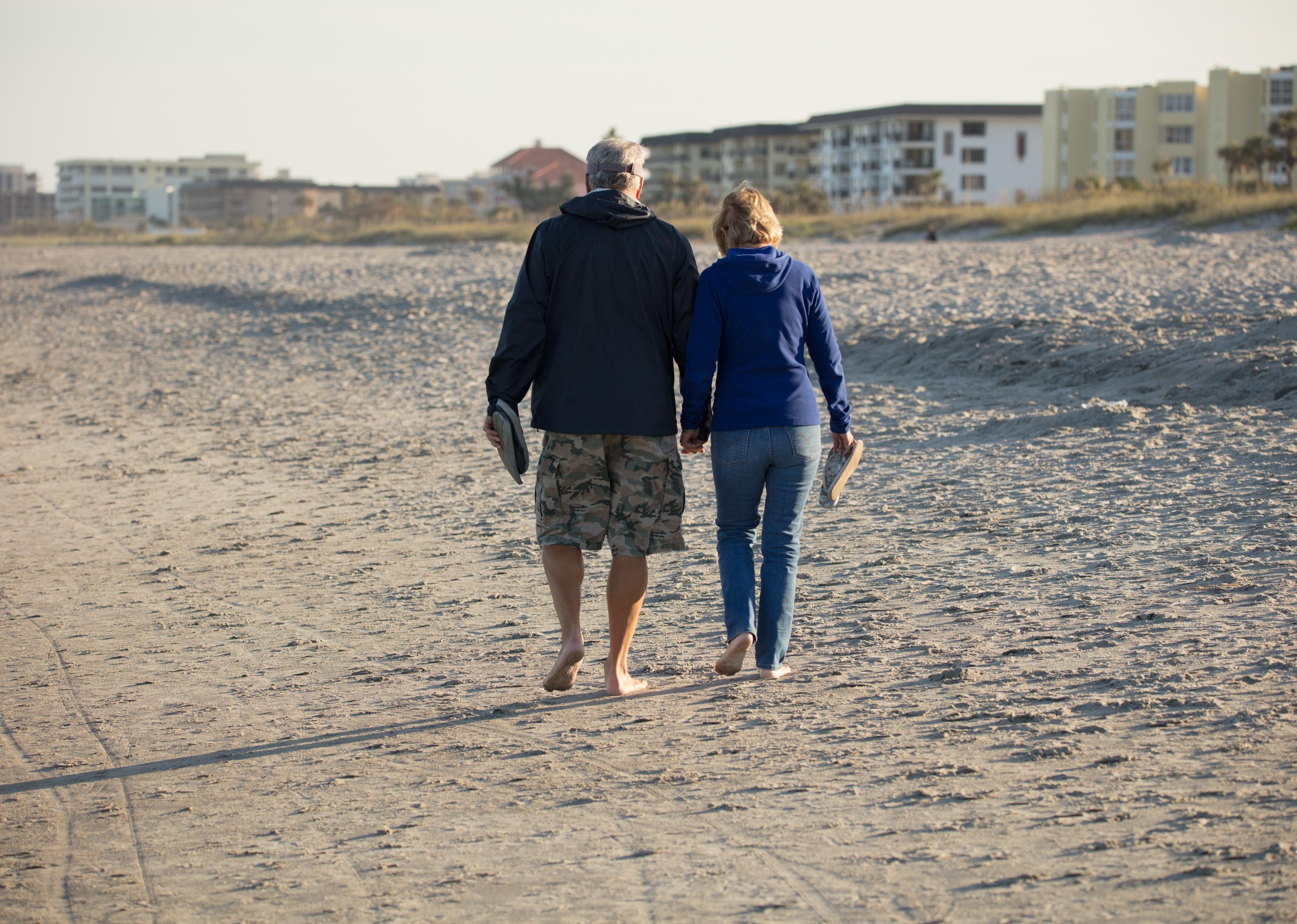 Senior couple holding hands walking on the beach.