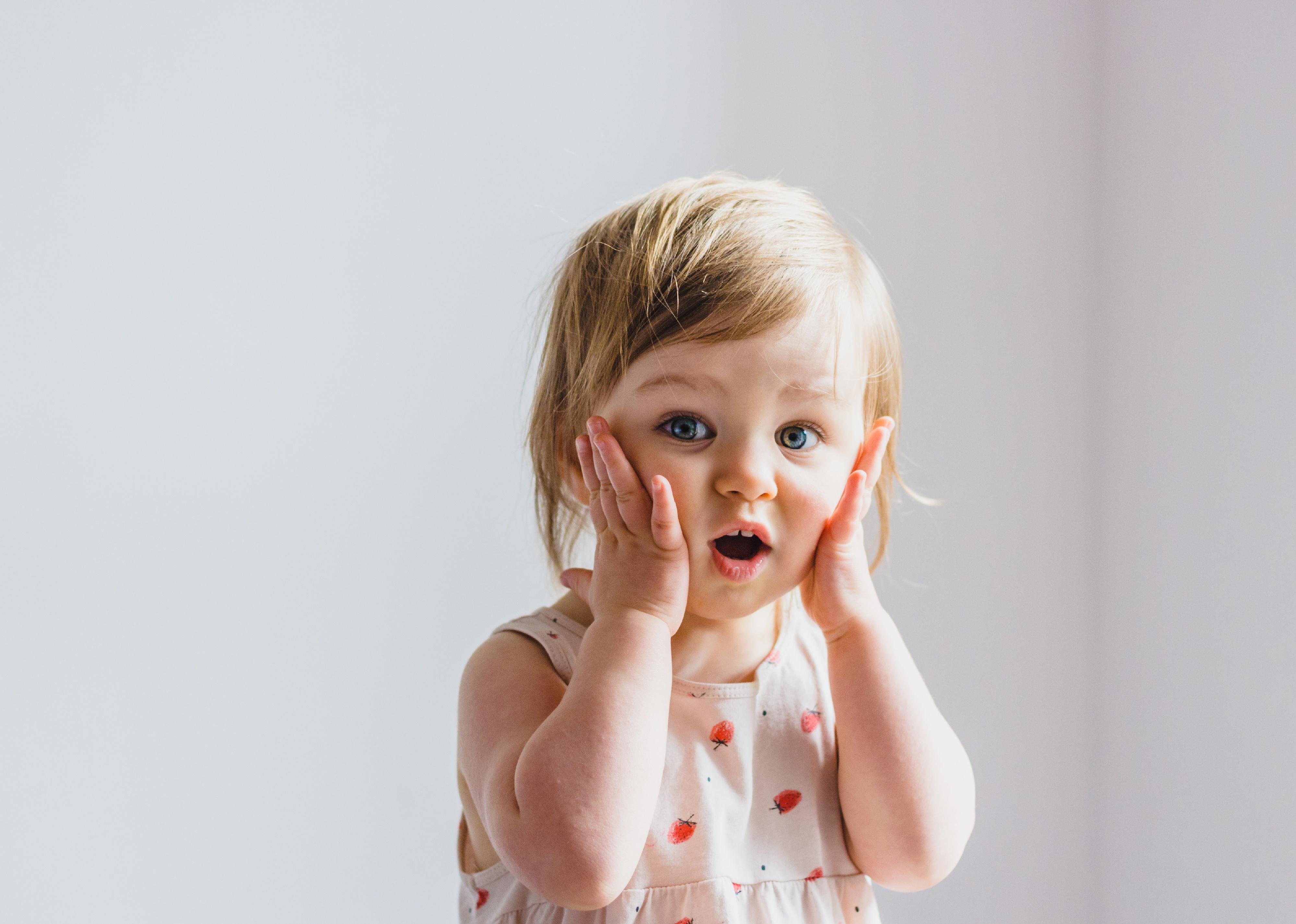 Surprised toddler with hands on her cheeks.