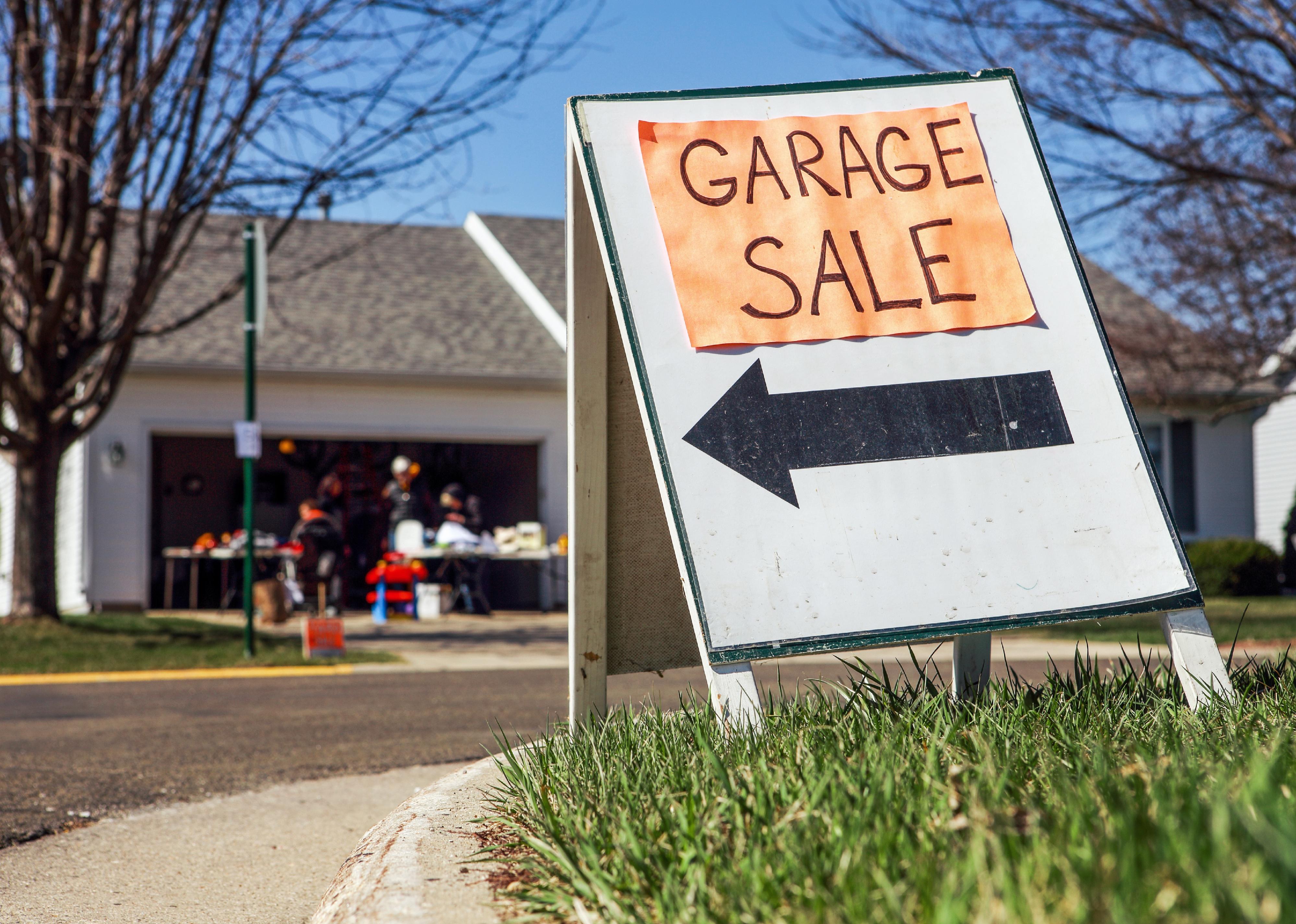 Garage sale sign on the lawn of a suburban home.