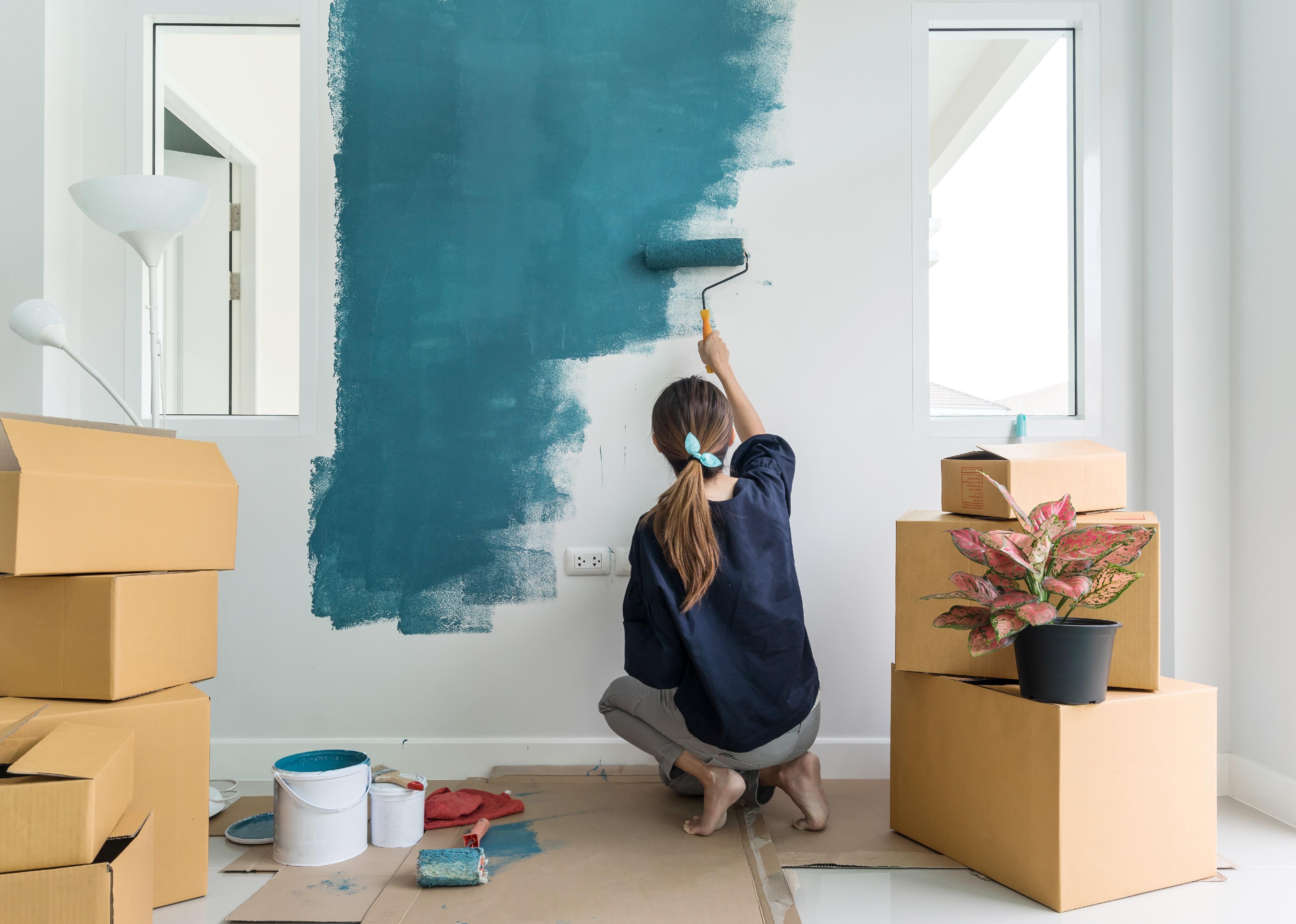Young woman painting interior wall with paint roller in new house.
