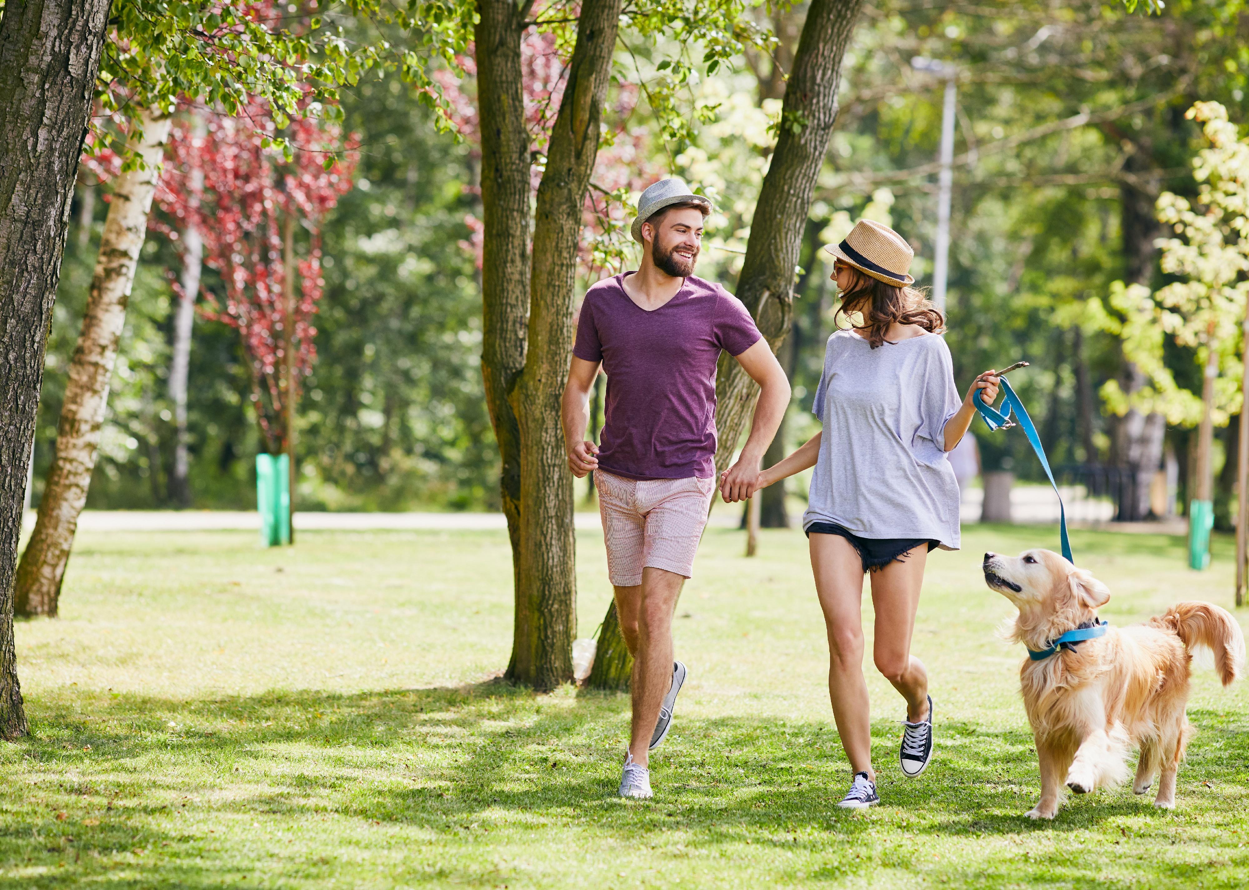 Young couple running in the park with their dog.