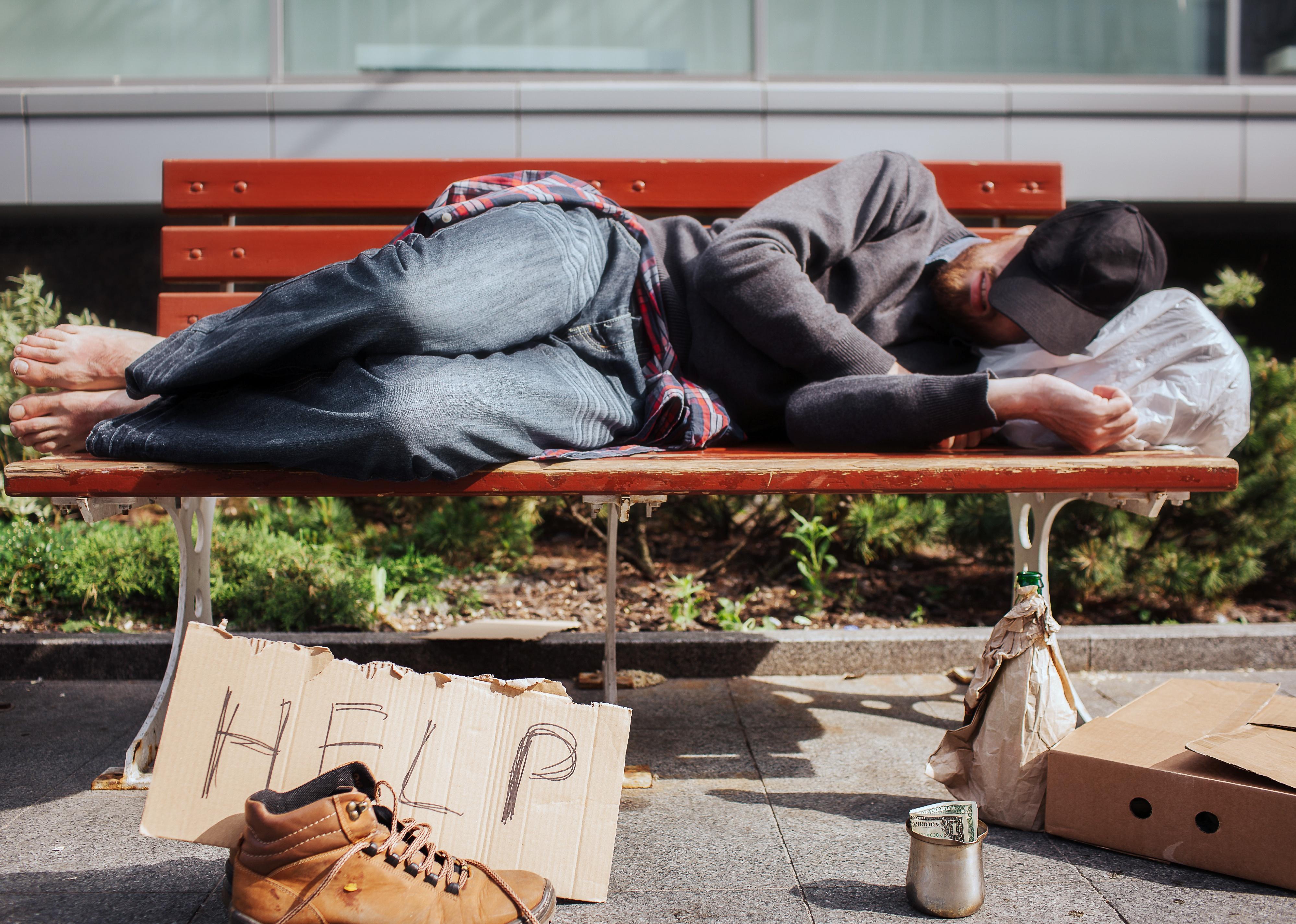 Homeless man is lying on bench and sleeping.