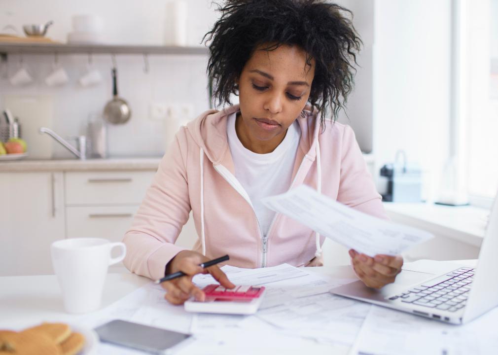 African American female sitting at kitchen table, using calculator and holding paper