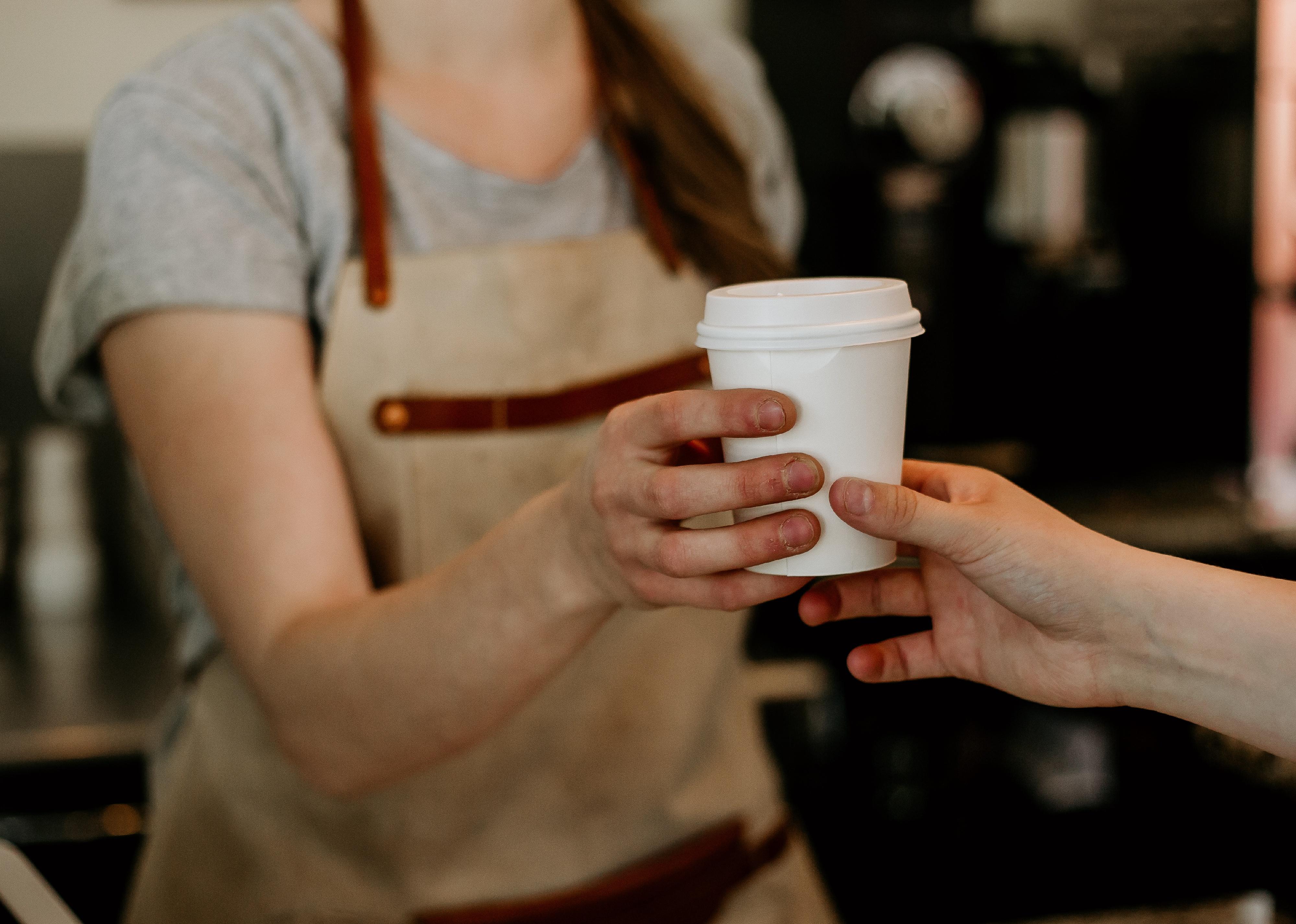 A barista handing a customer a cup of to go coffee.