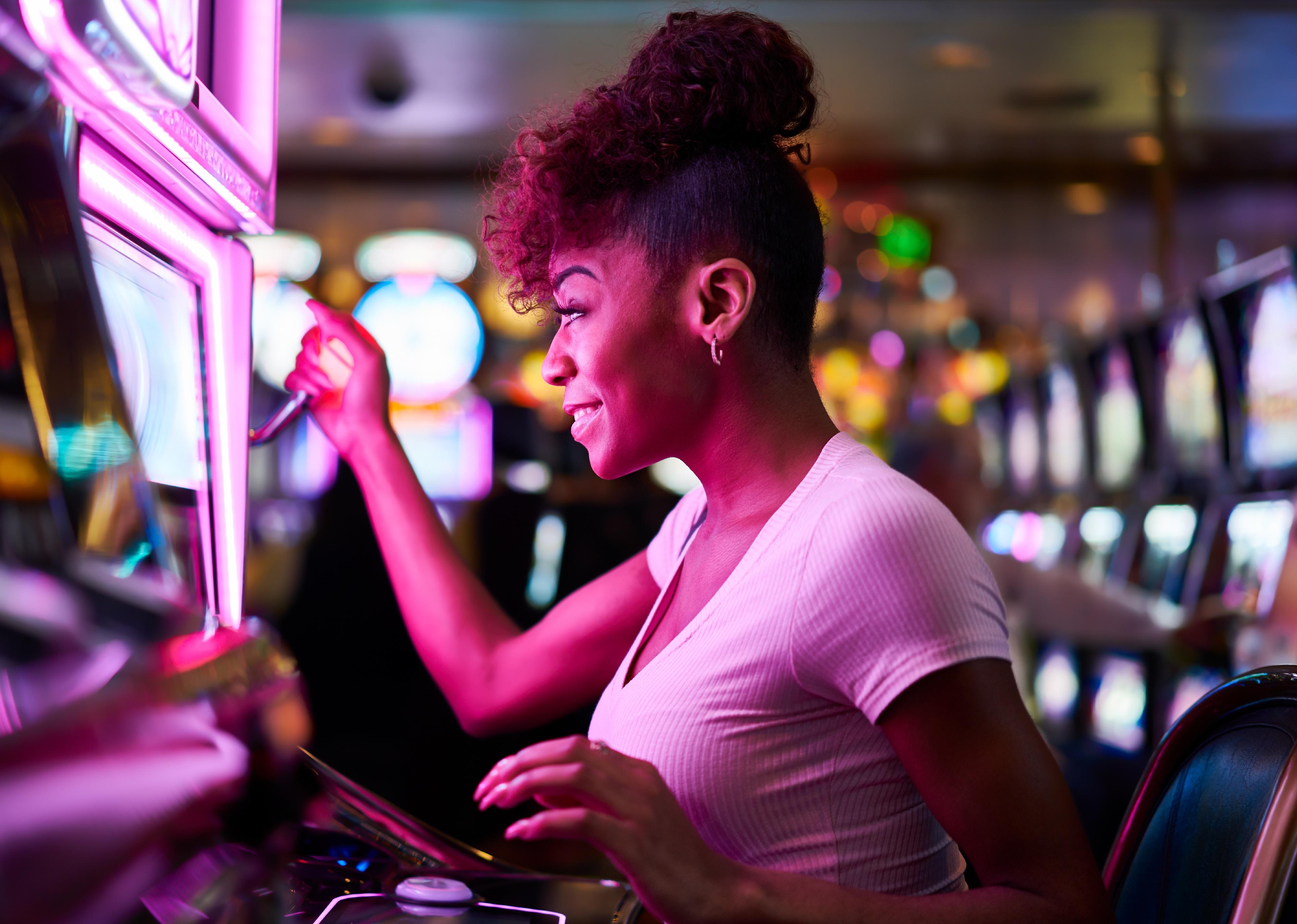 Happy woman gambling at casino playing slot machine.