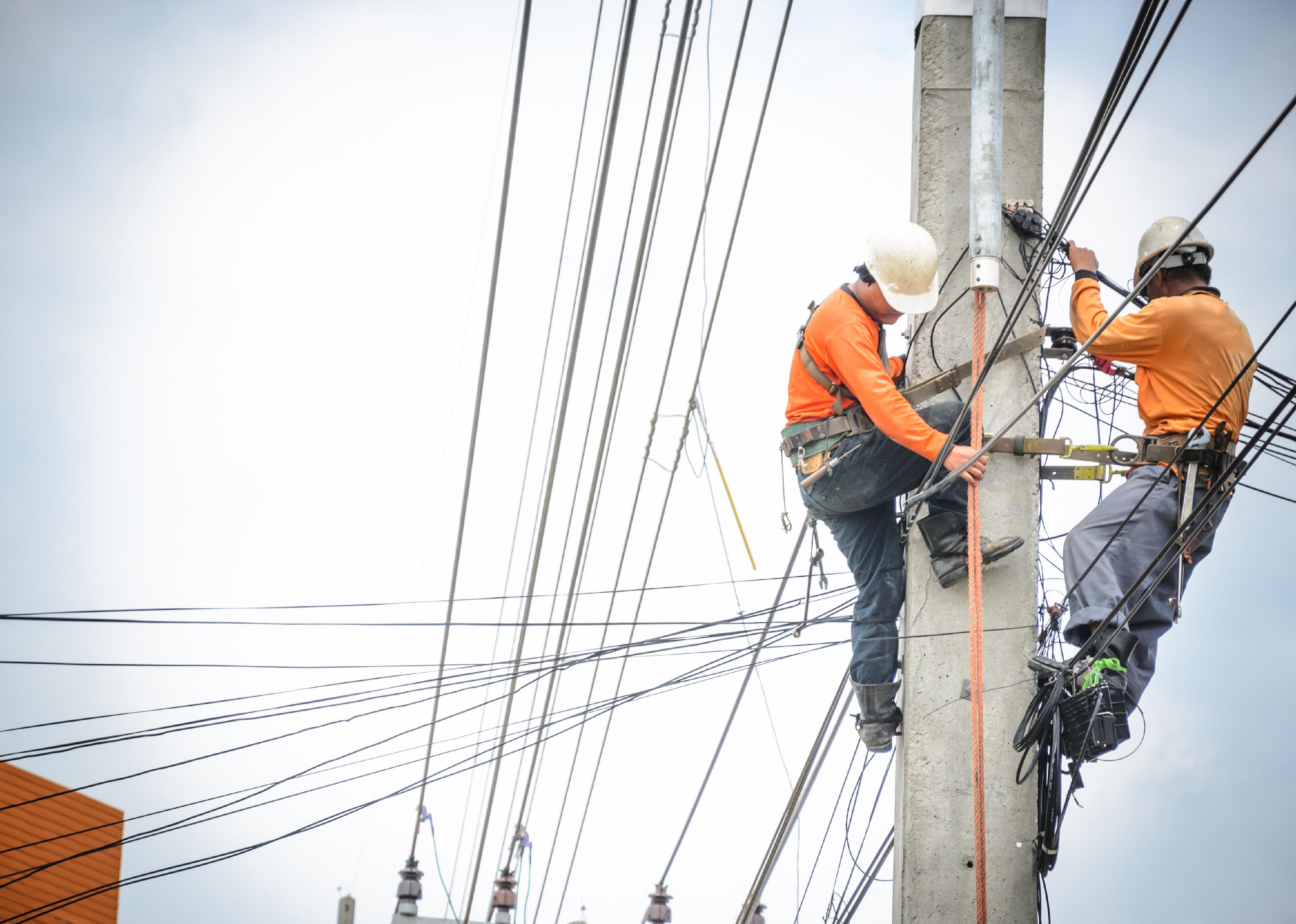 Electricians climbing on electric poles to repair power lines.