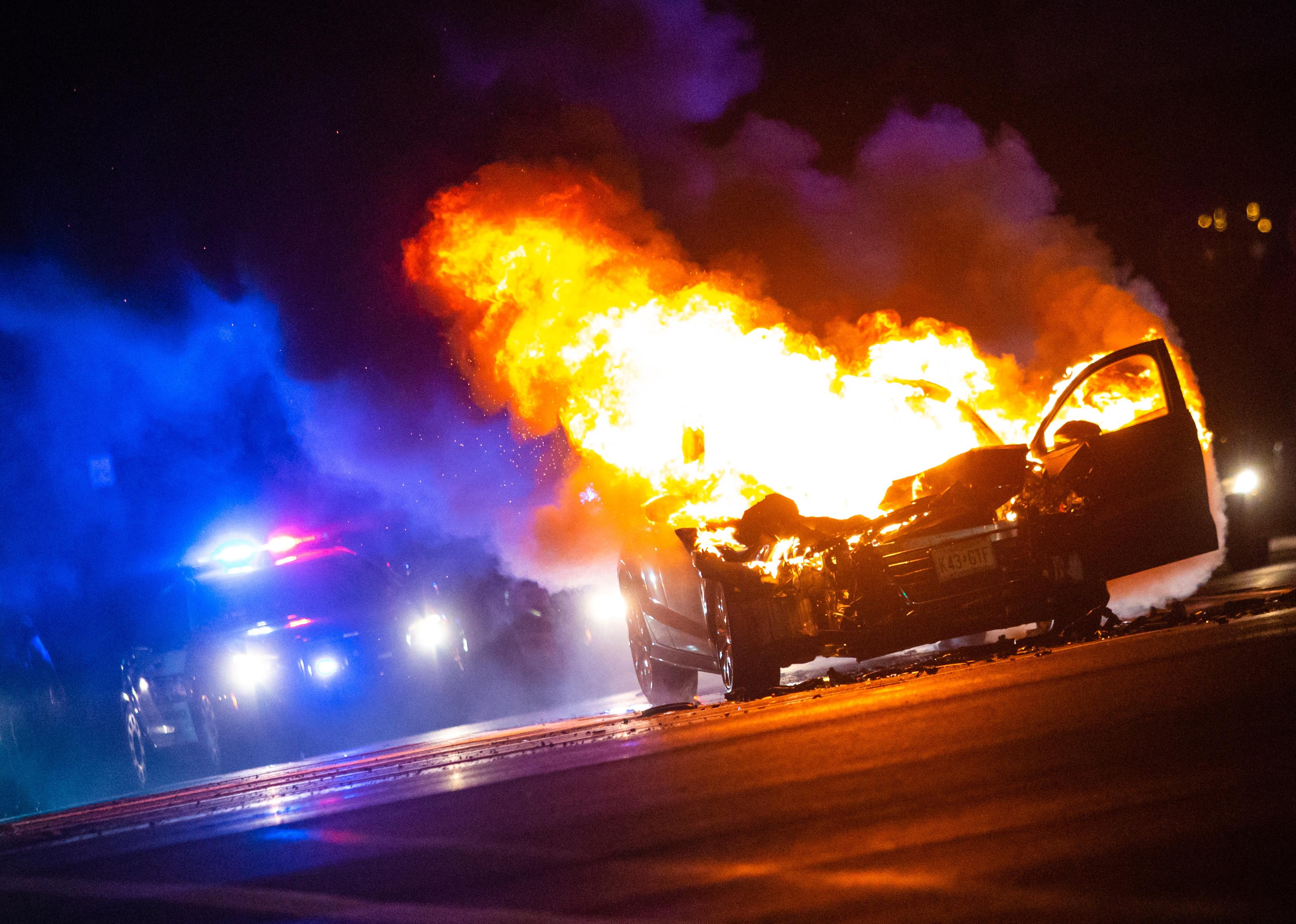 Car on fire at night with police lights in background.
