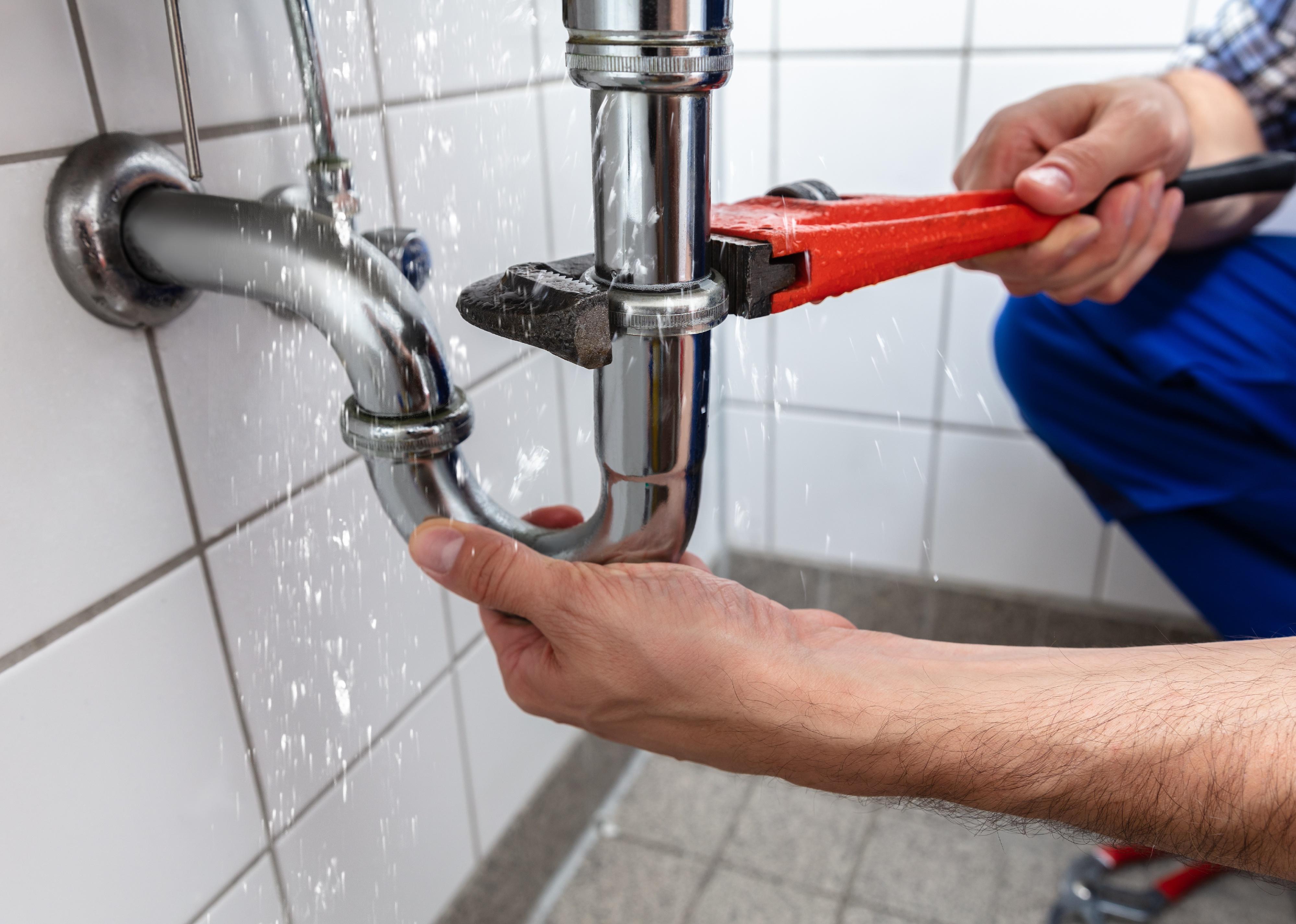 Plumber's hand repairing sink with wrench.