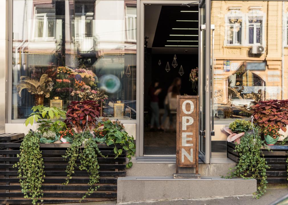 Open signboard, potted plants and reflecting windows at flower shop