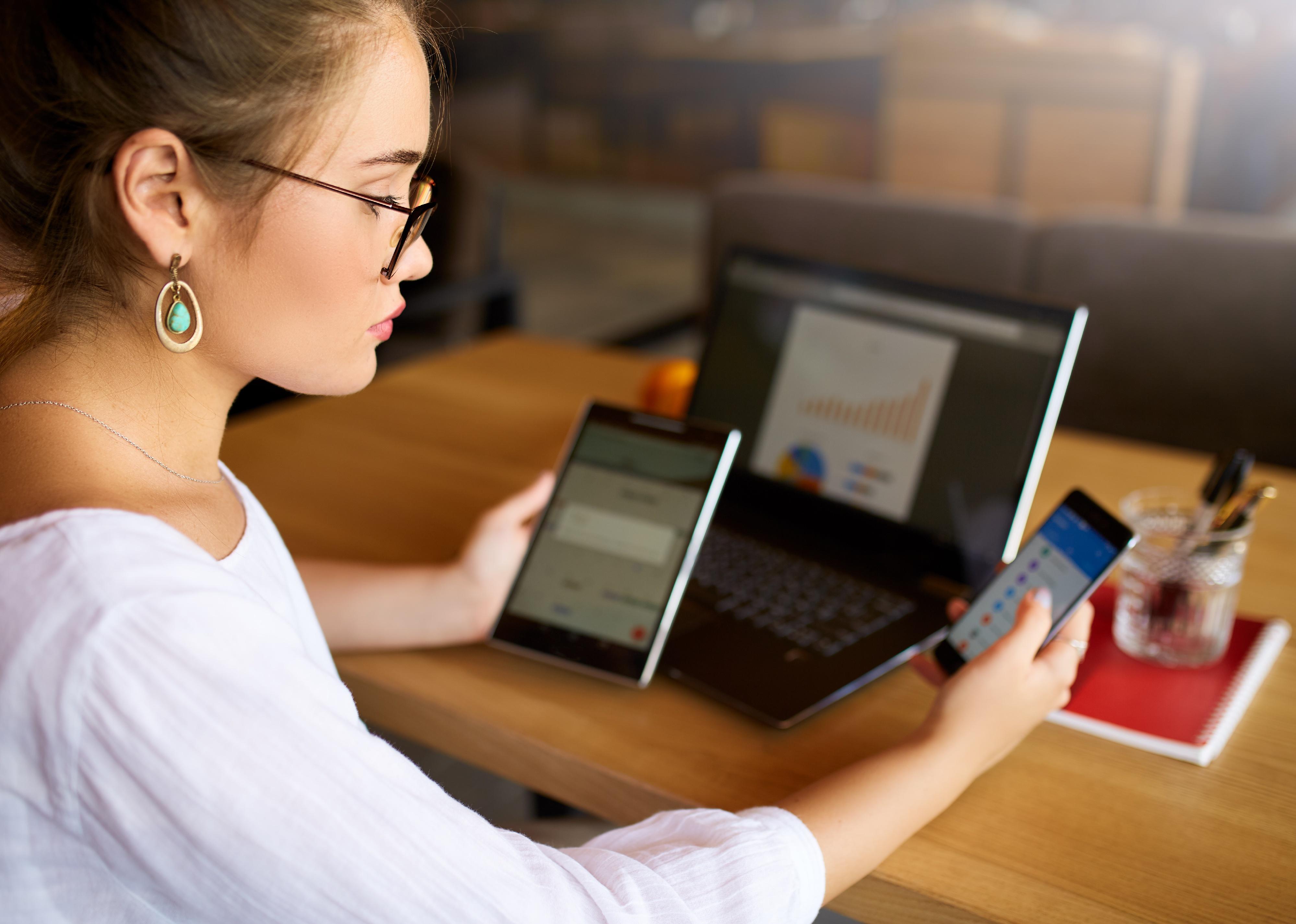 Woman in glasses working with multiple electronic internet devices.