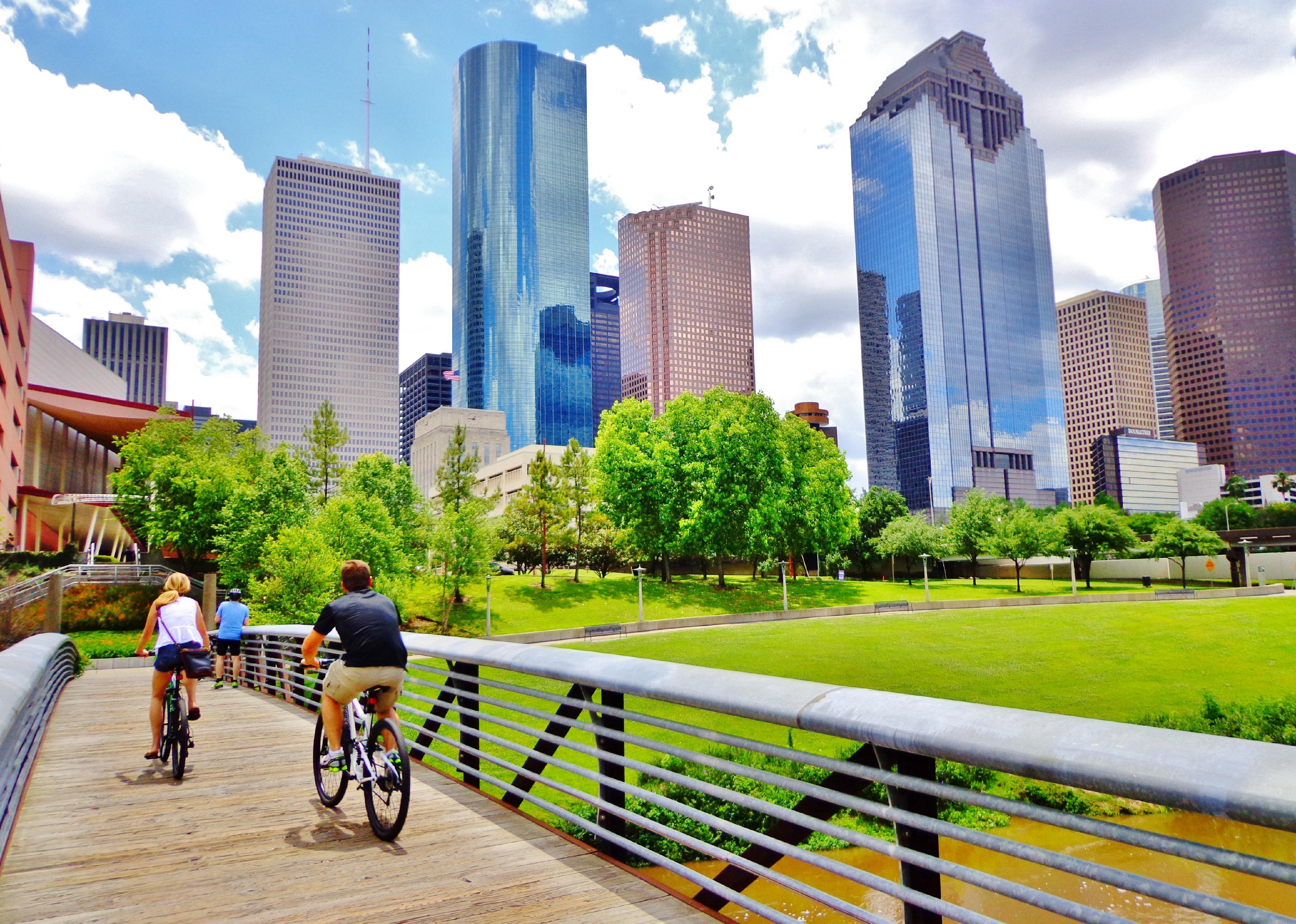 Bicyclists ride on a small bridge with a view of downtown Houston.