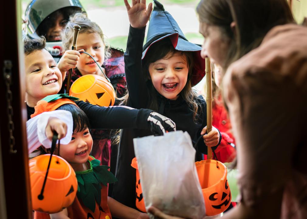 A person greets happy children at their front door, trick or treating on Halloween.