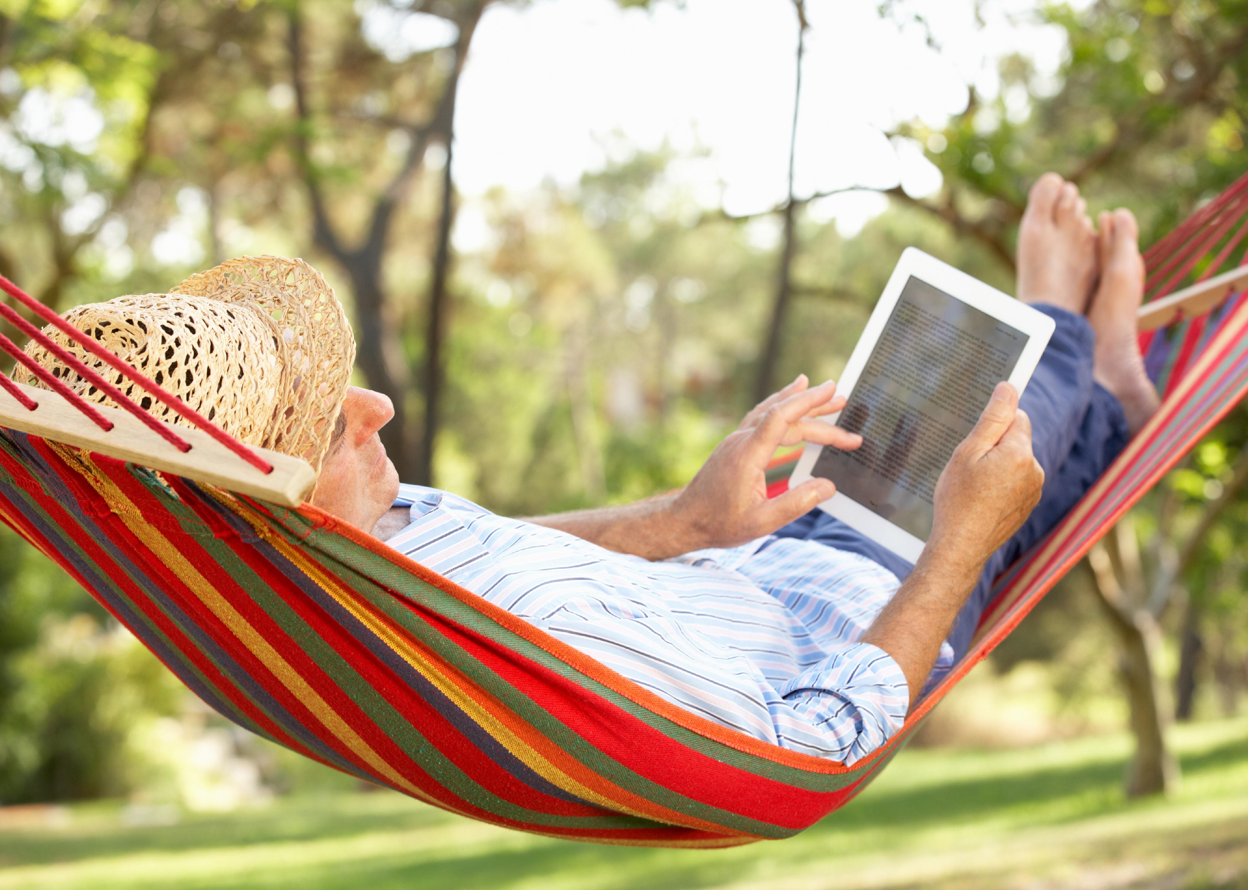 Senior relaxing in hammock with e-book.