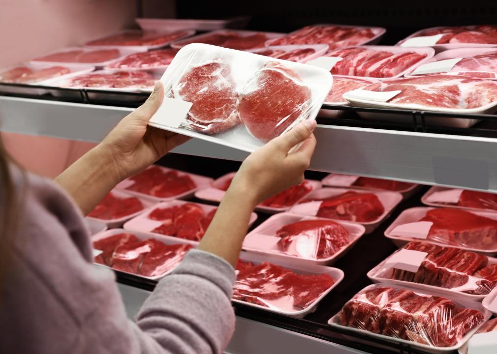 Woman taking packed pork meat from shelf in supermarket.