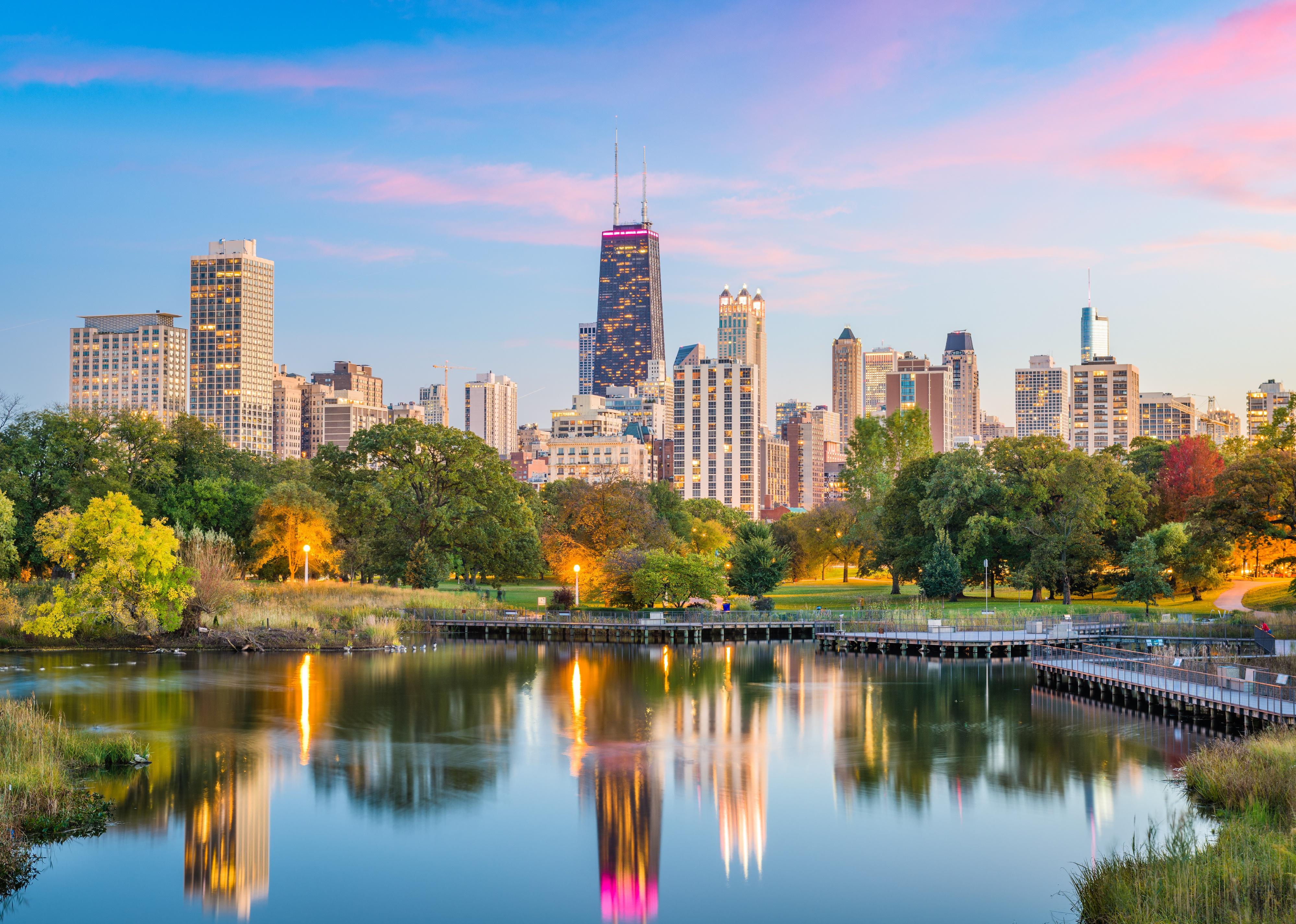 The Chicago skyline with a blue and pink sky in the background and reflective water in the foreground.
