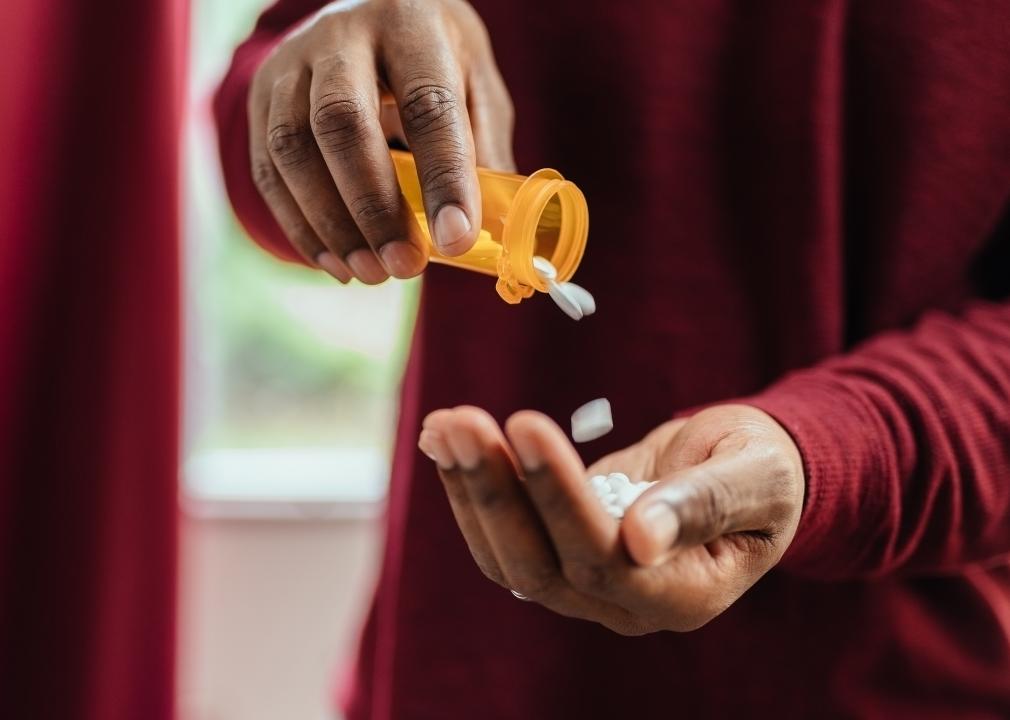 Person in red shirt pouring pills from prescription pill bottle into his hand.