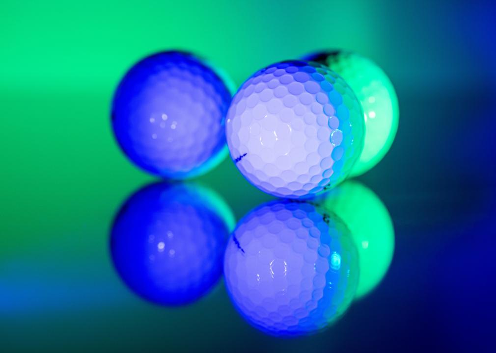 Three white golf balls illuminated in bright green and blue