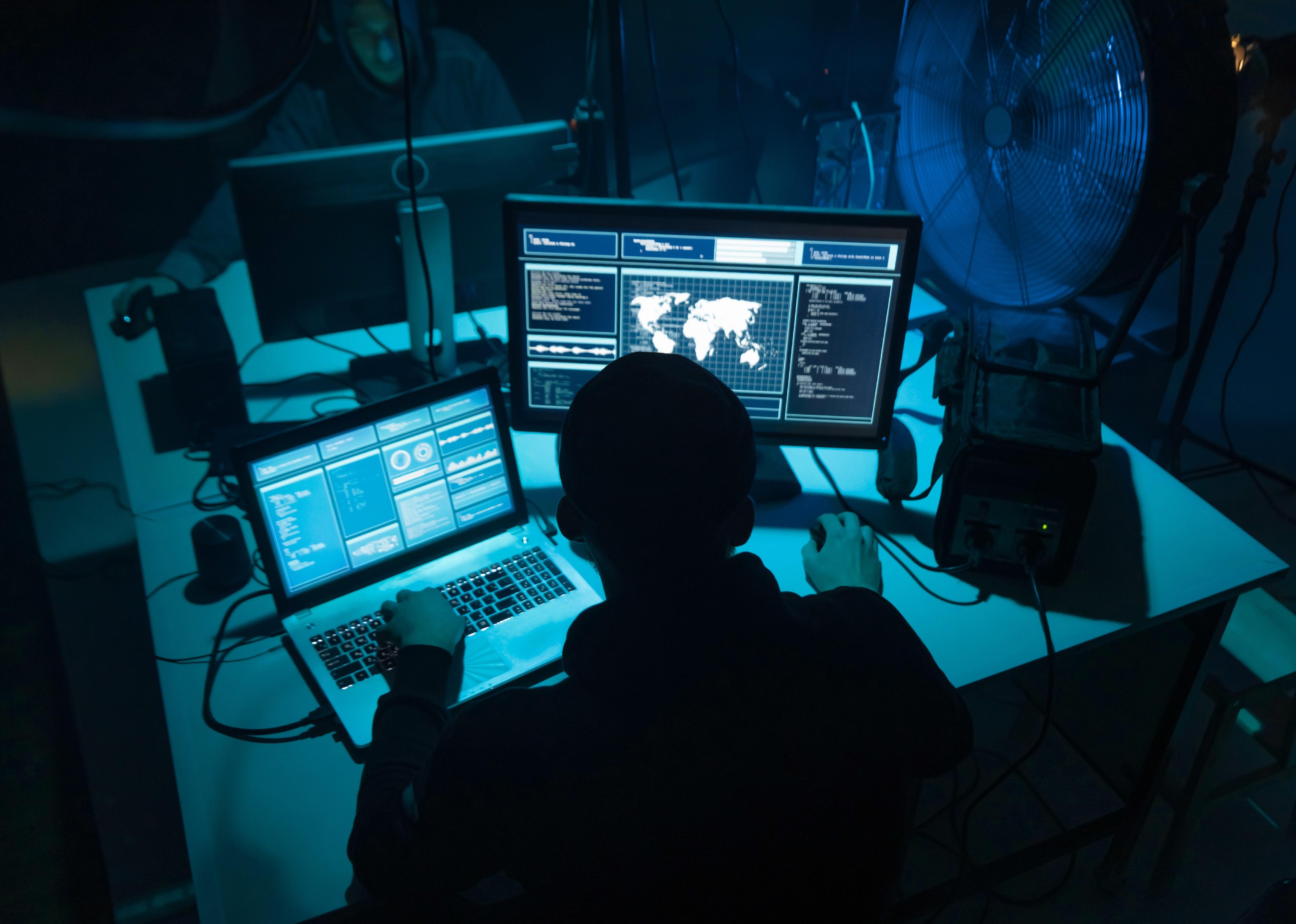 Dark room with hacker coding virus ransomware using laptops and computers.