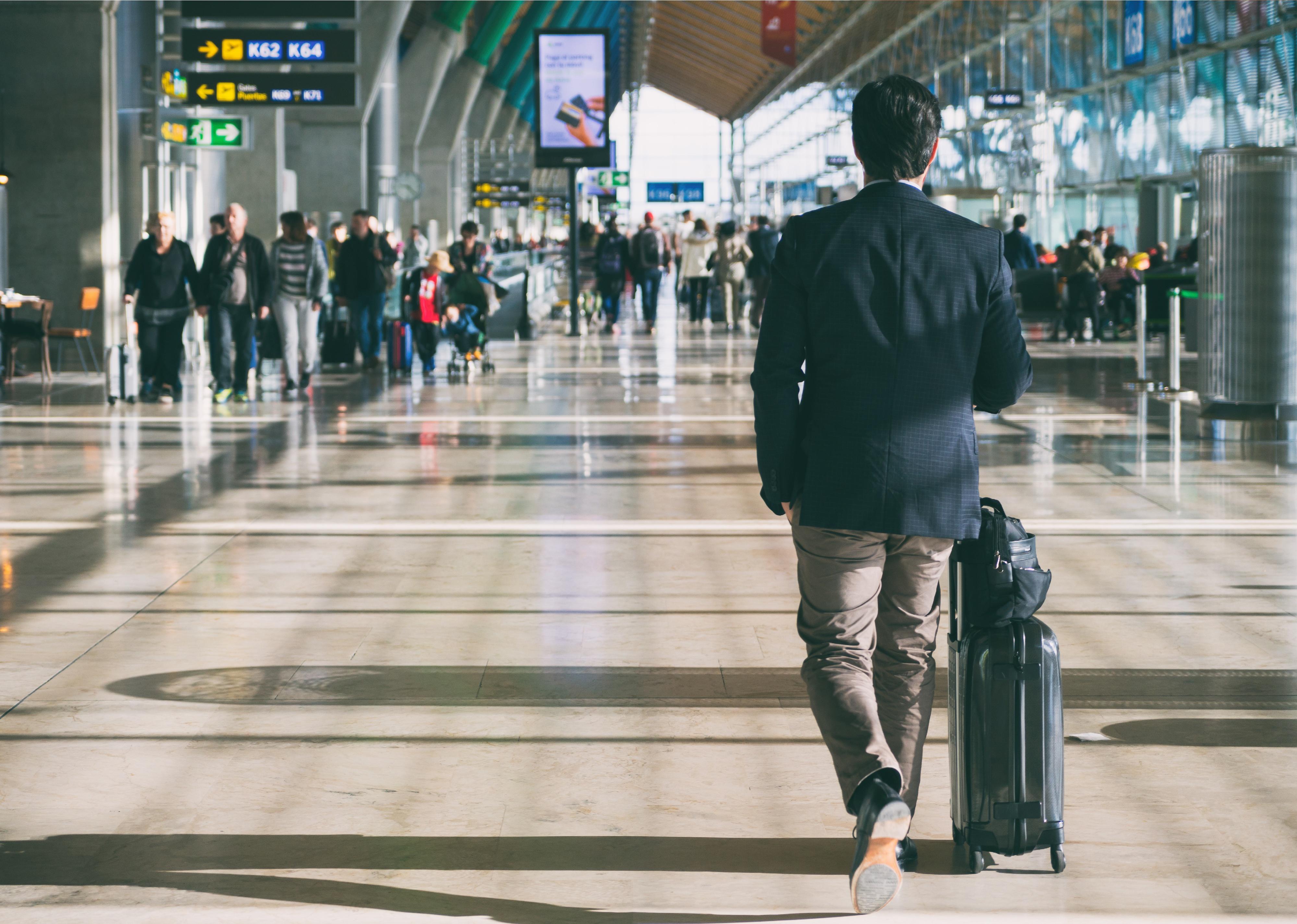 Businessperson rolling a suitcase while walking through an airport.