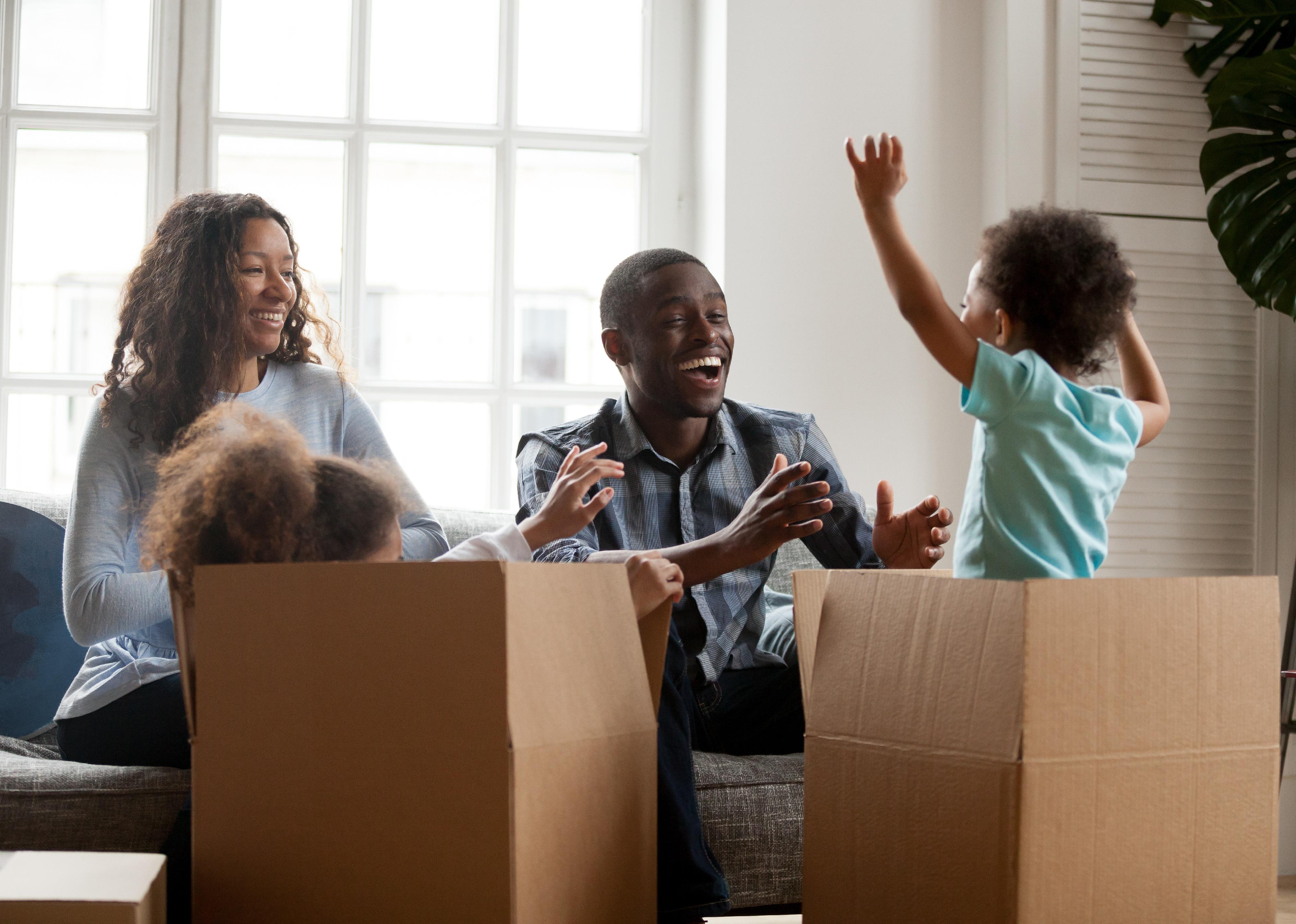 Excited kids jumping out of box playing with parents in living room