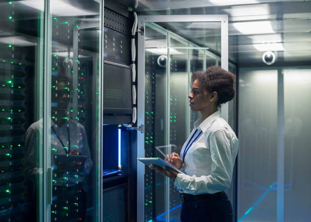 Woman technician working on a tablet in a data center full of rack servers.