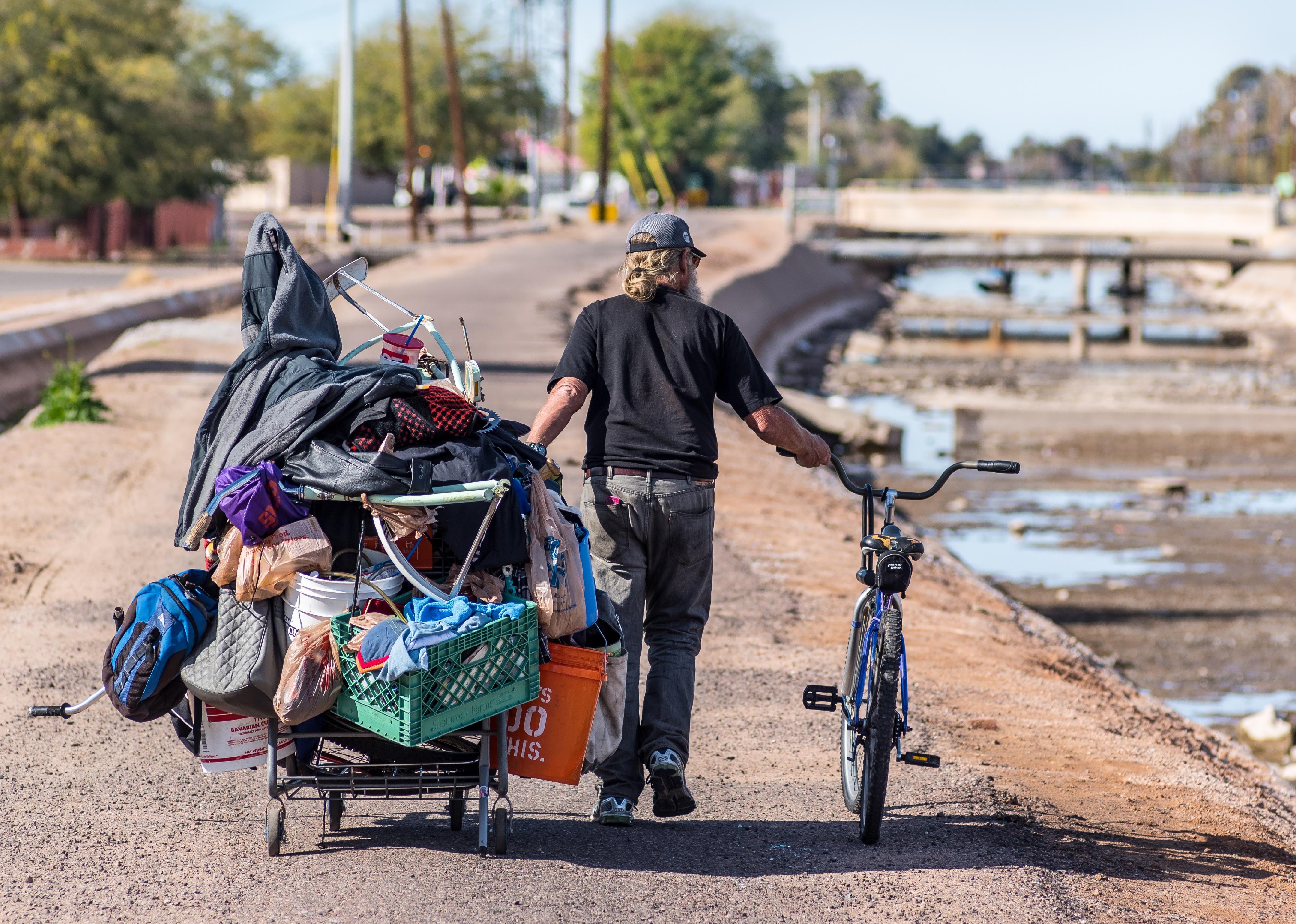 A homeless man pulls an overladen shopping cart along a path next to the Arizona Canal.