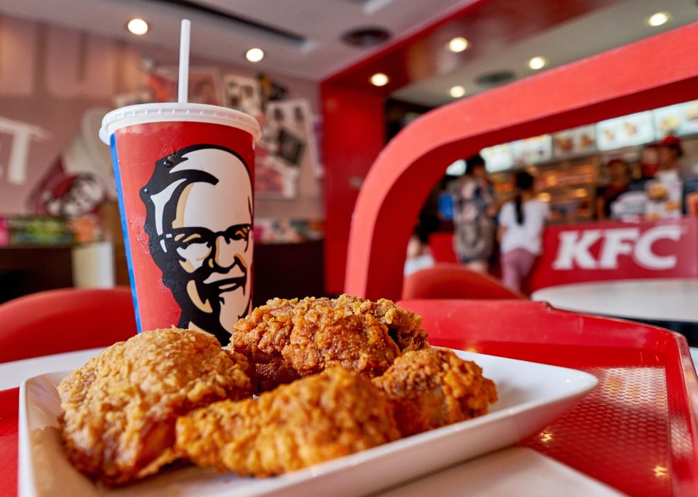 A close up of fried chicken on a plate and a drink with Colonel Sanders' face on it on a red tray in a KFC.