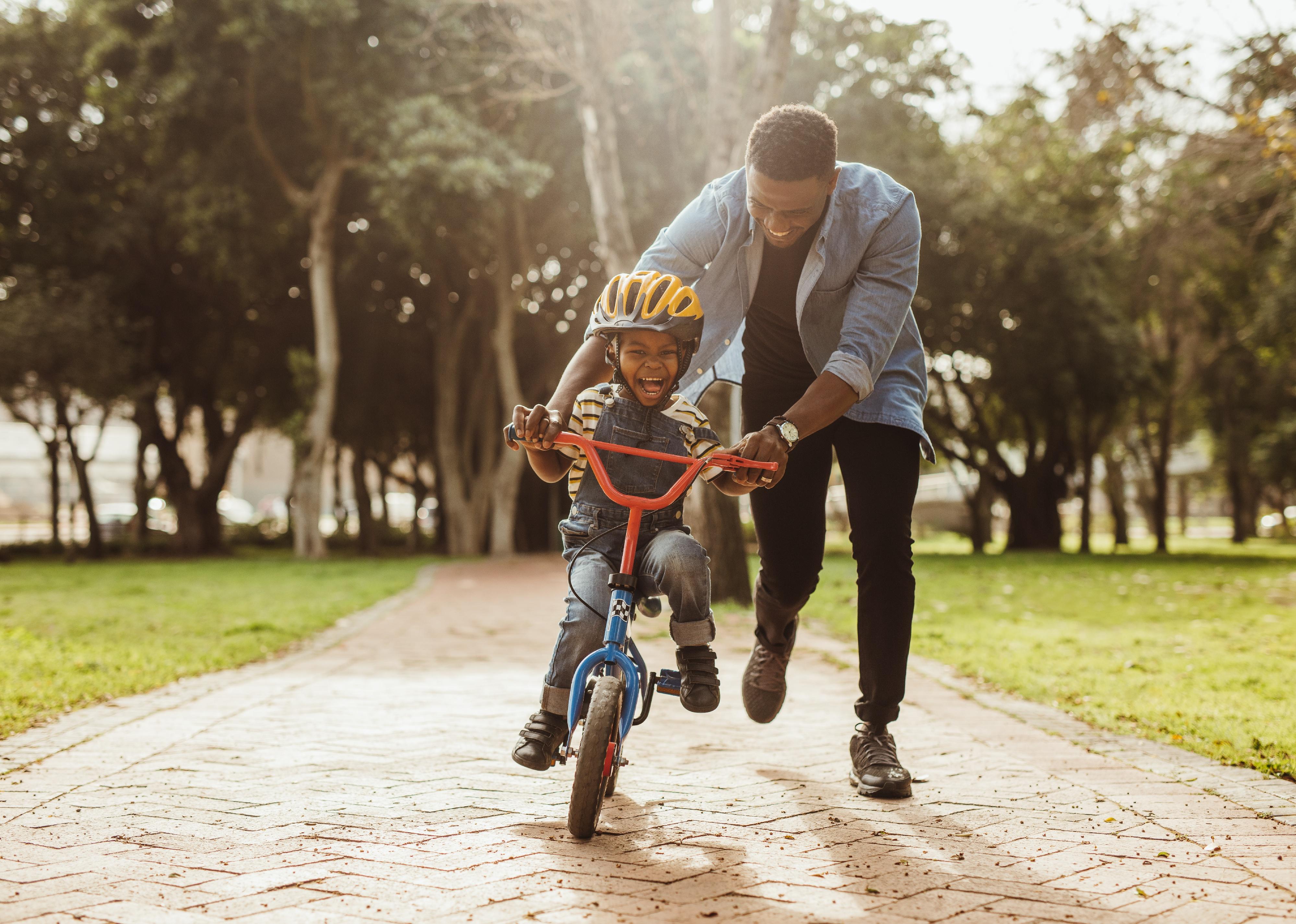 Boy learning to ride a bicycle with his father in park.