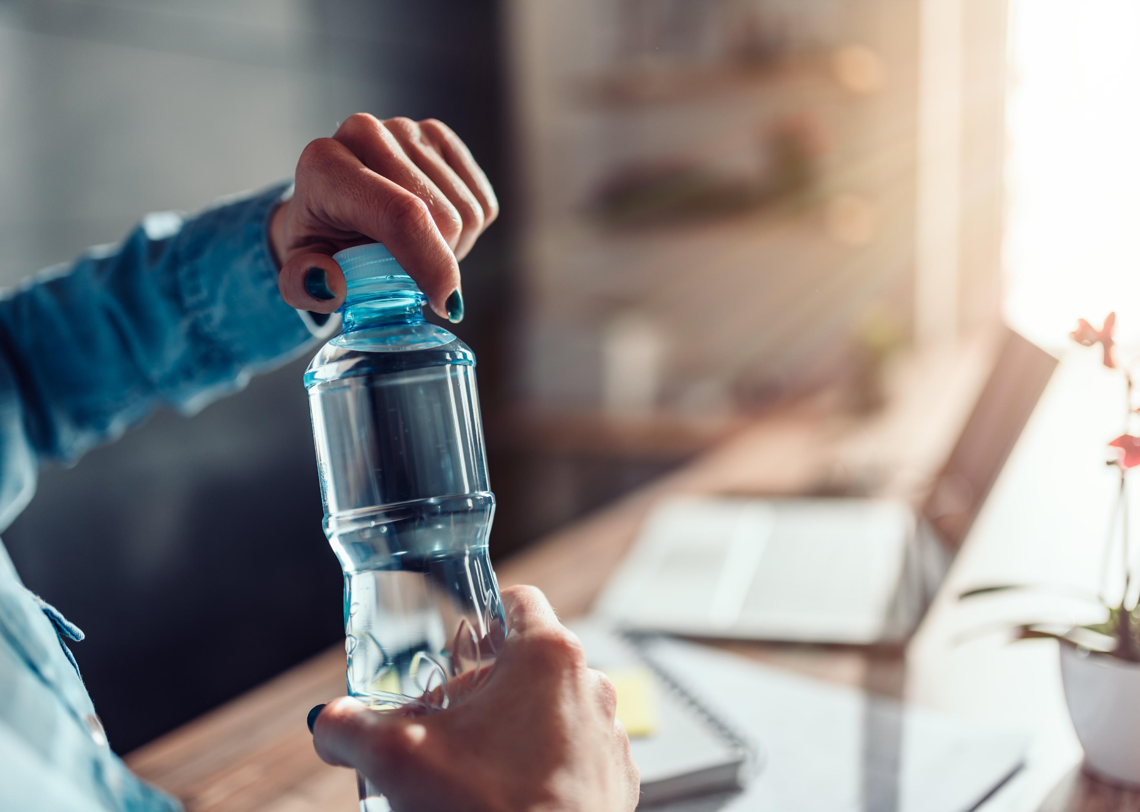 Person wearing denim shirt working in the office and opening plastic bottle of water.