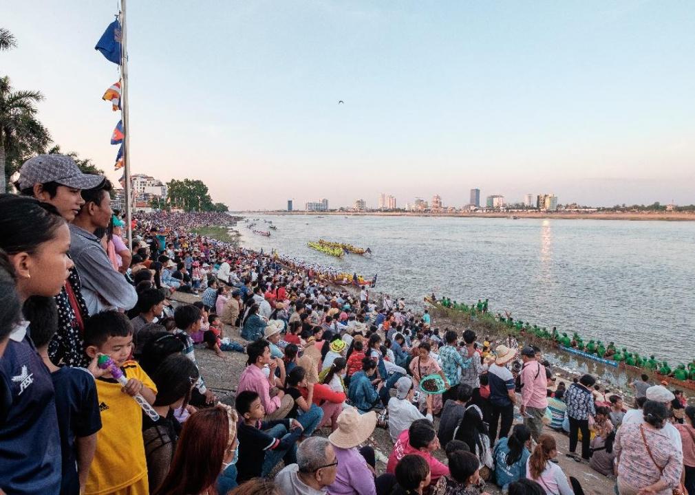 Crowds of people line the shore of the river.