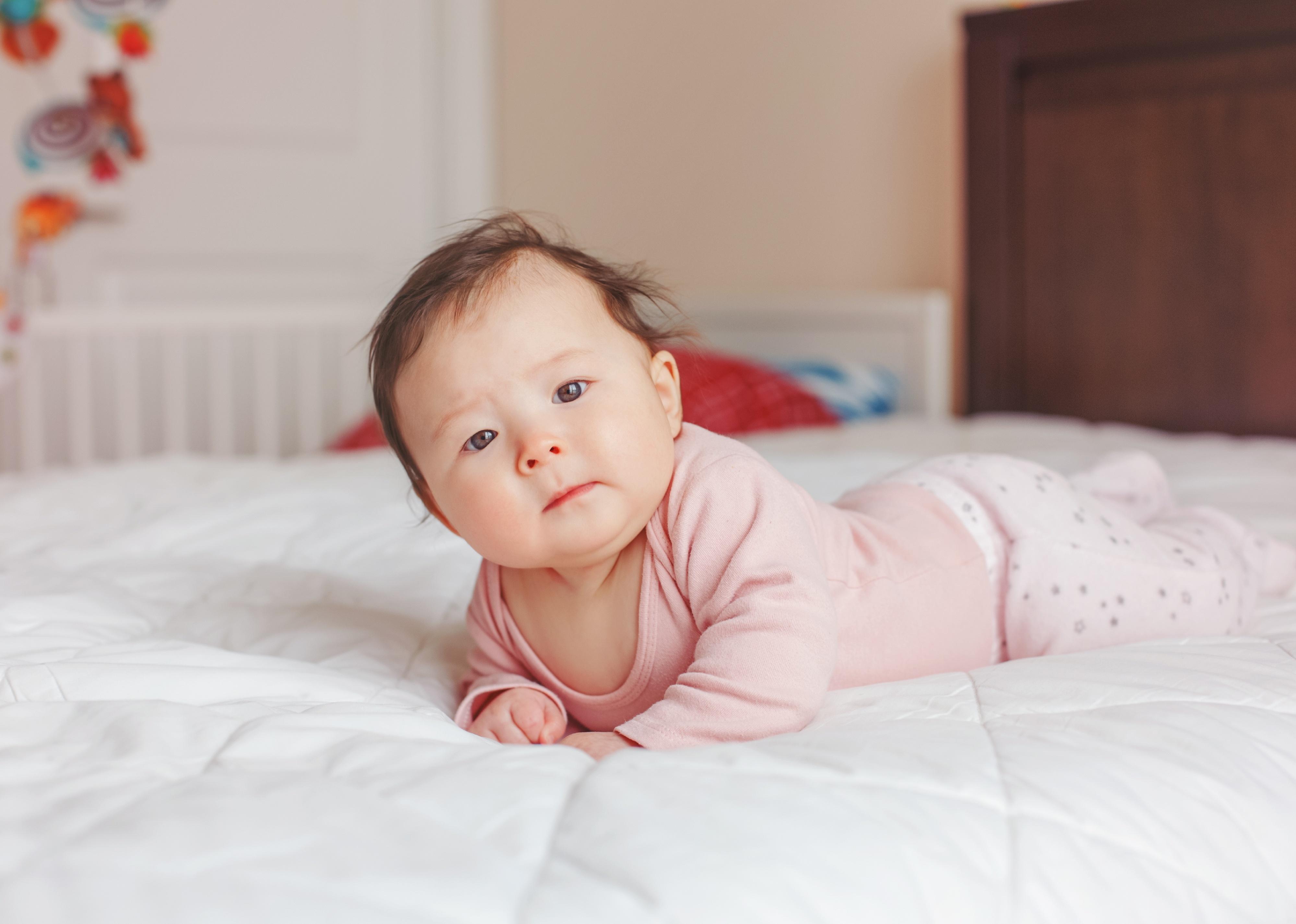 Baby girl laying on tummy on white bedding.