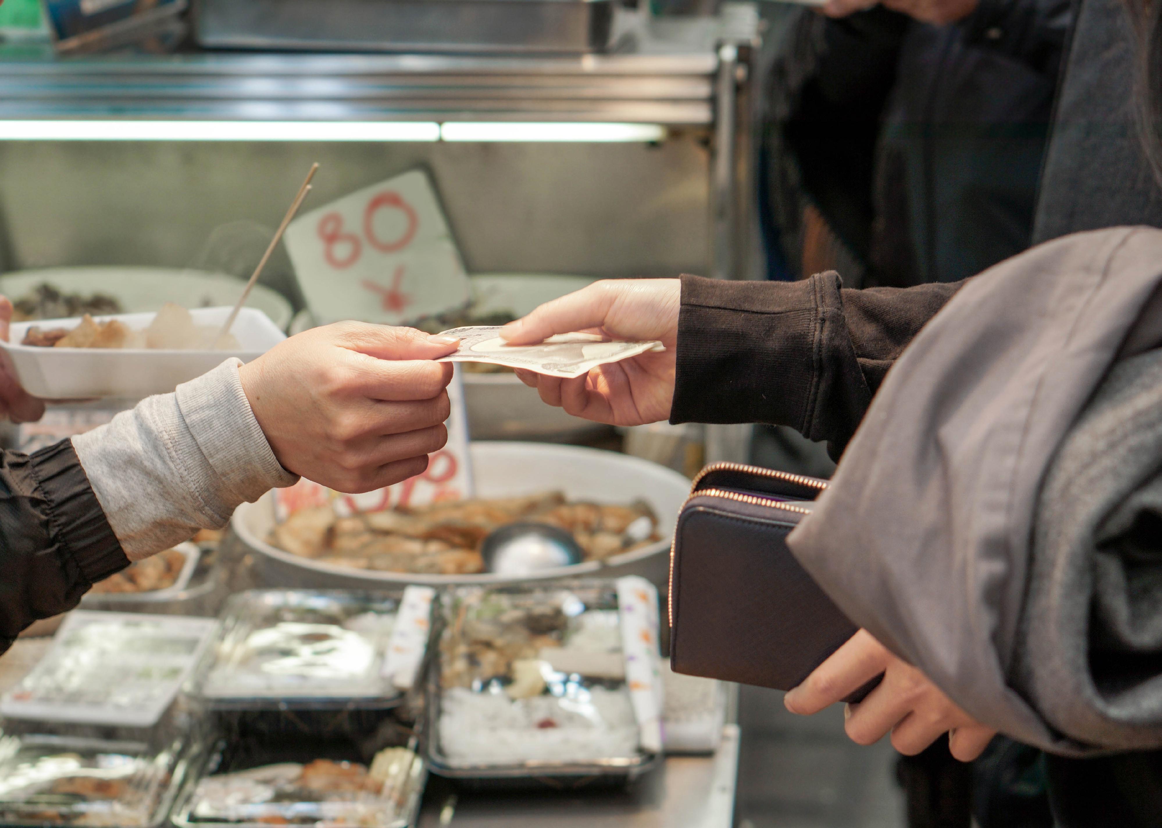 Closeup of customer paying with Japan yen banknote for food in the market.