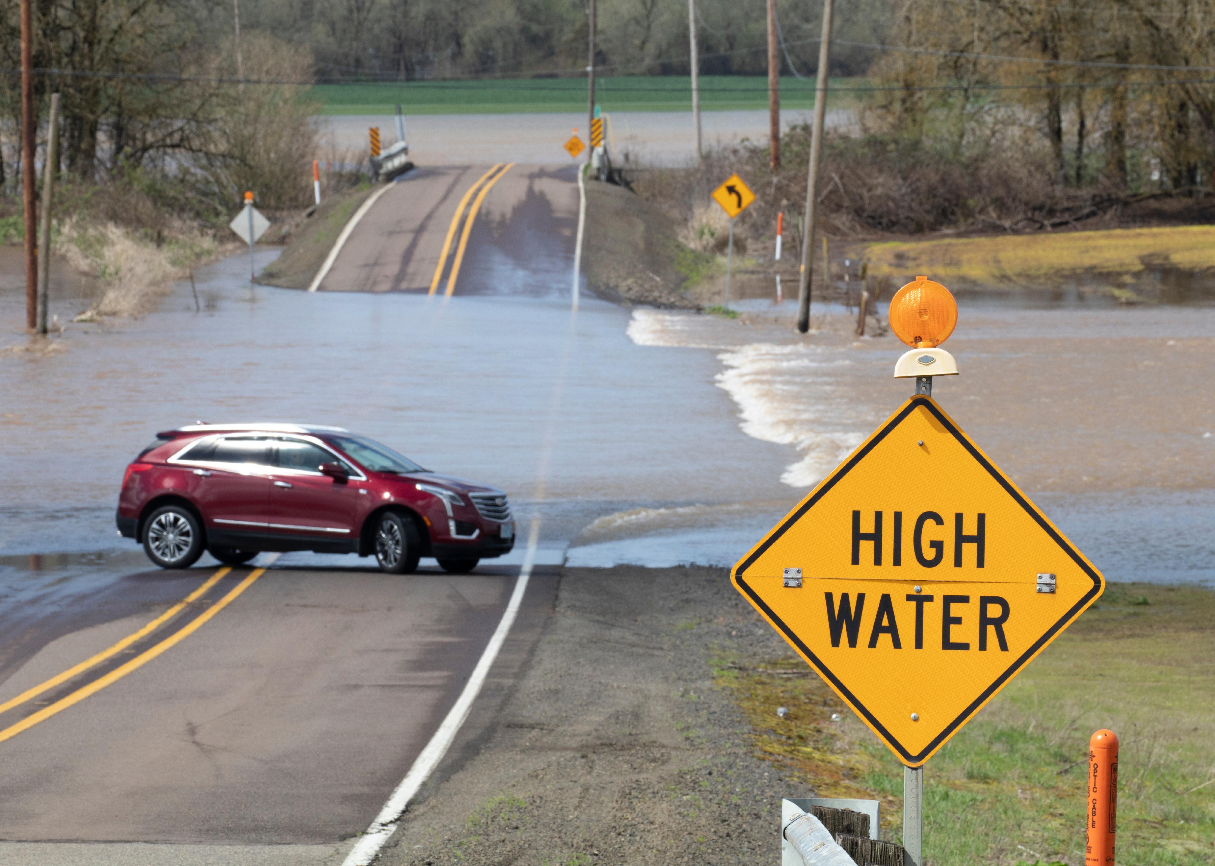 A car turns around after encountering a flooded field streaming across a rural road.