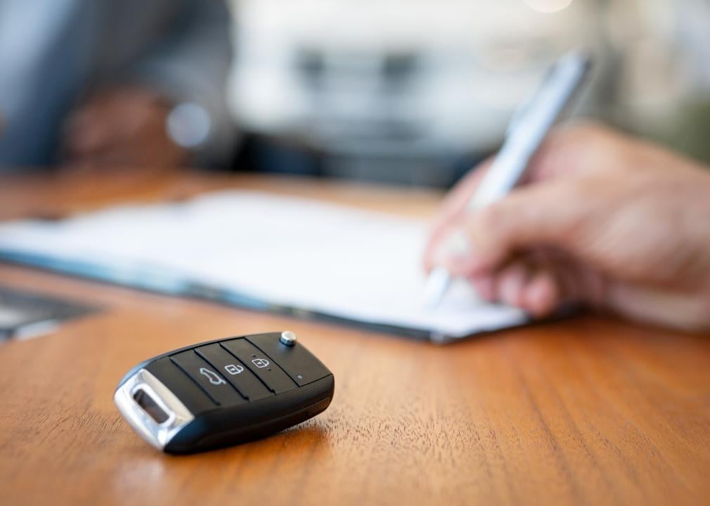 Car keys on desk with man signing purchase documents in background