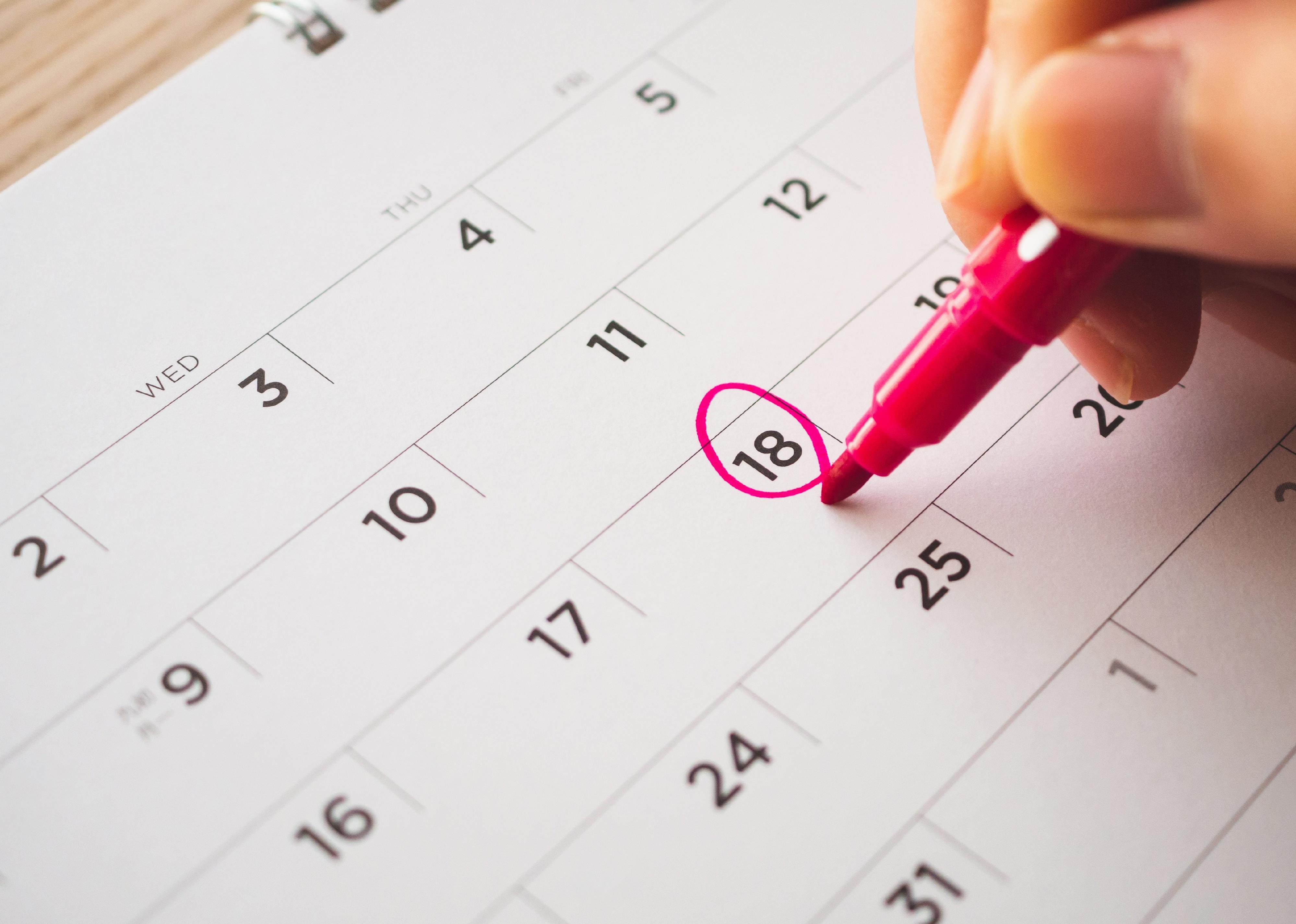 Person using pen to mark on calendar date.