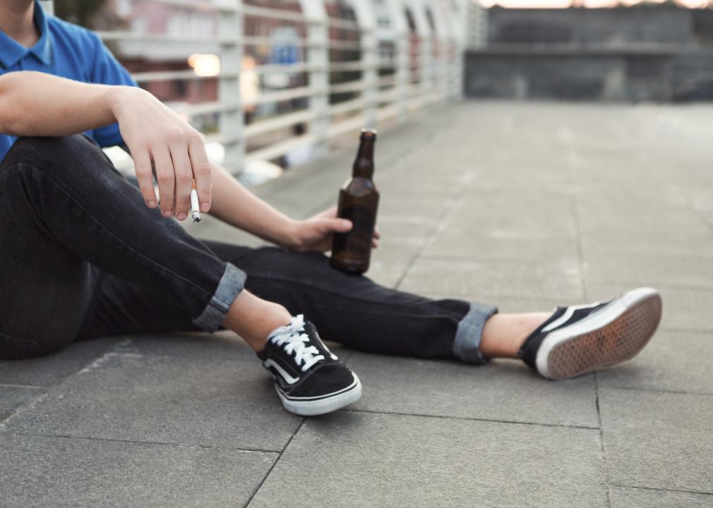 Teen smoking cigarette and drinking beer on a rooftop.