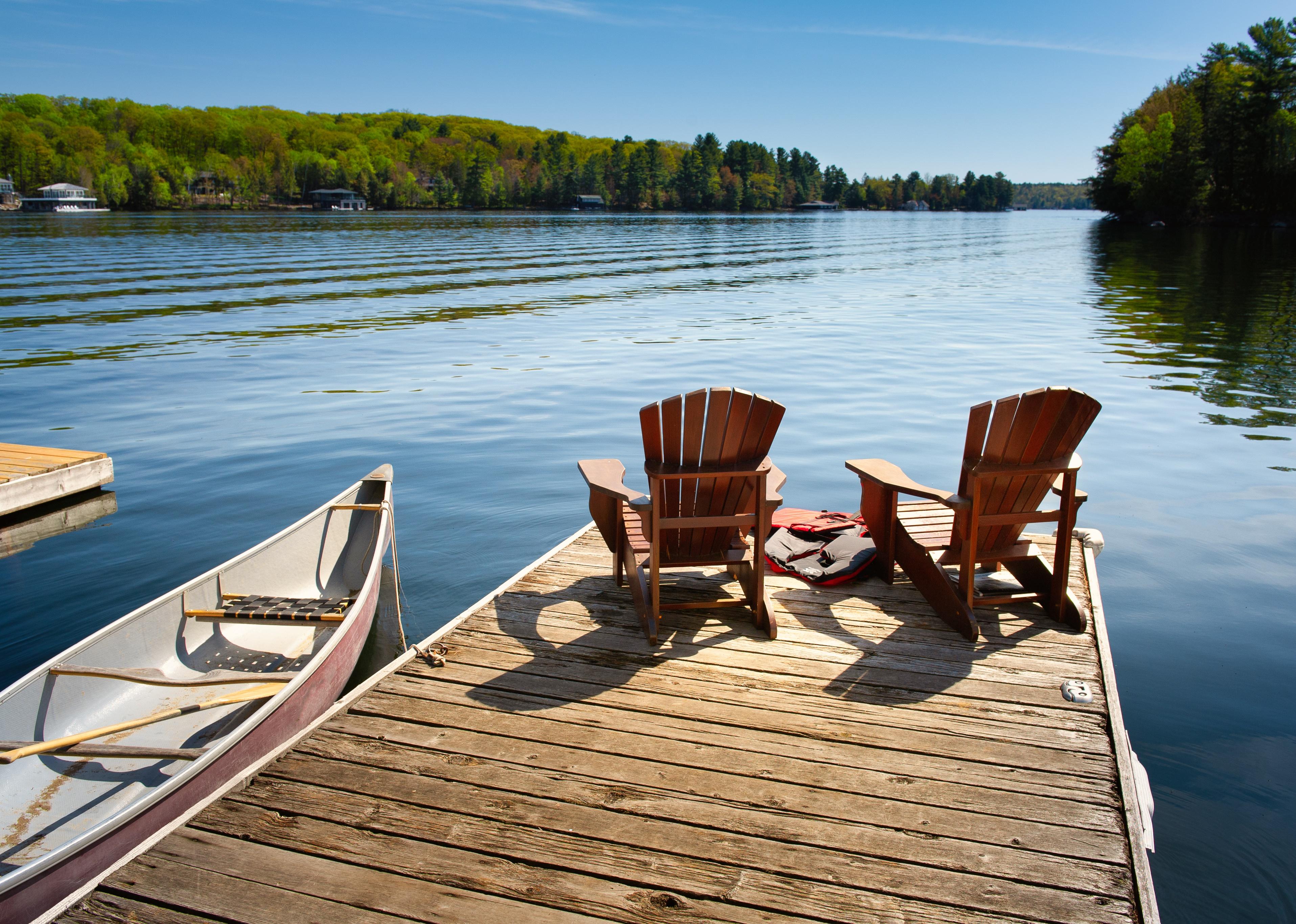 Two Adirondack chairs on a wooden dock facing the blue water.