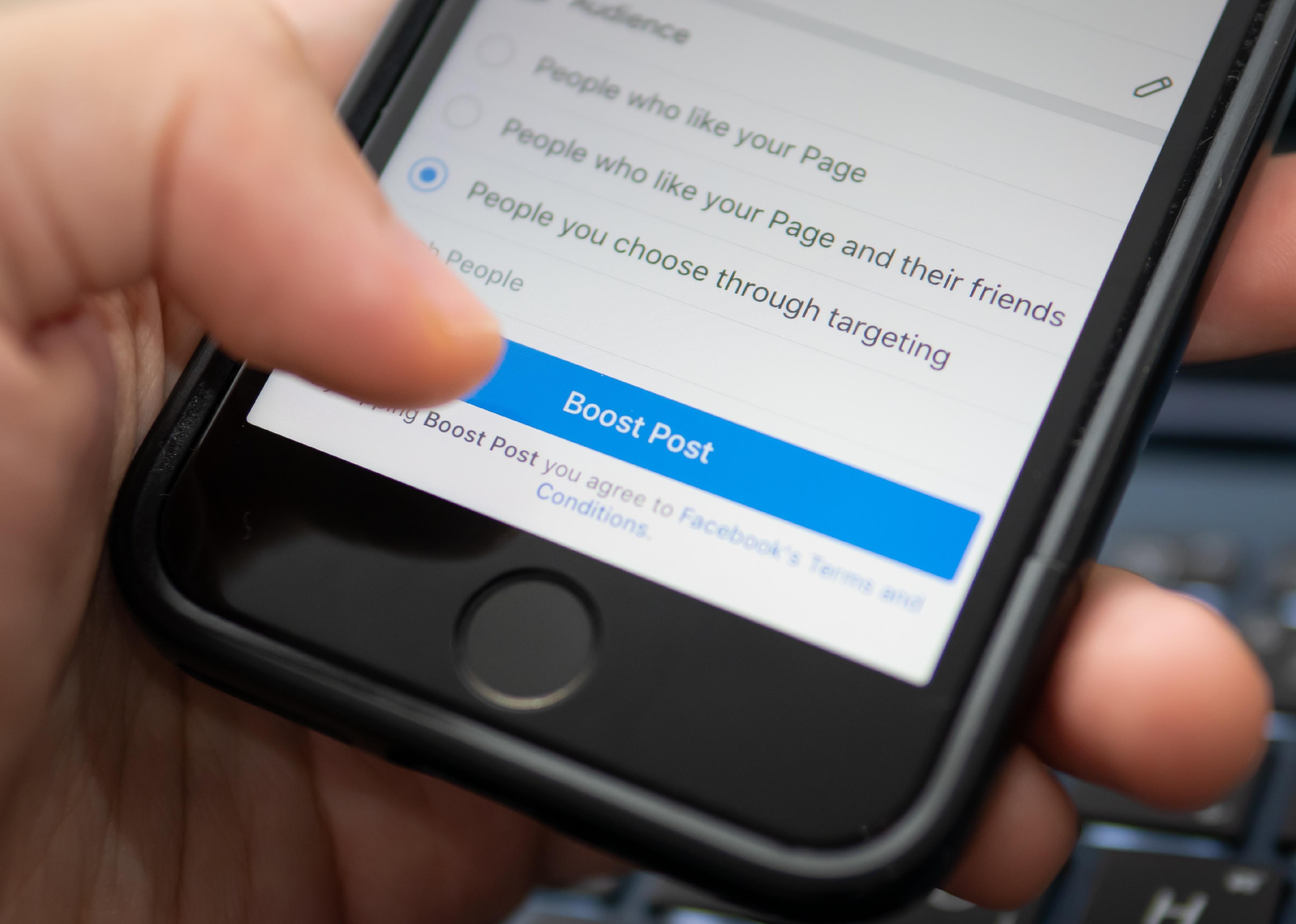 Hand touching the "Boost Post" button on Facebook App.