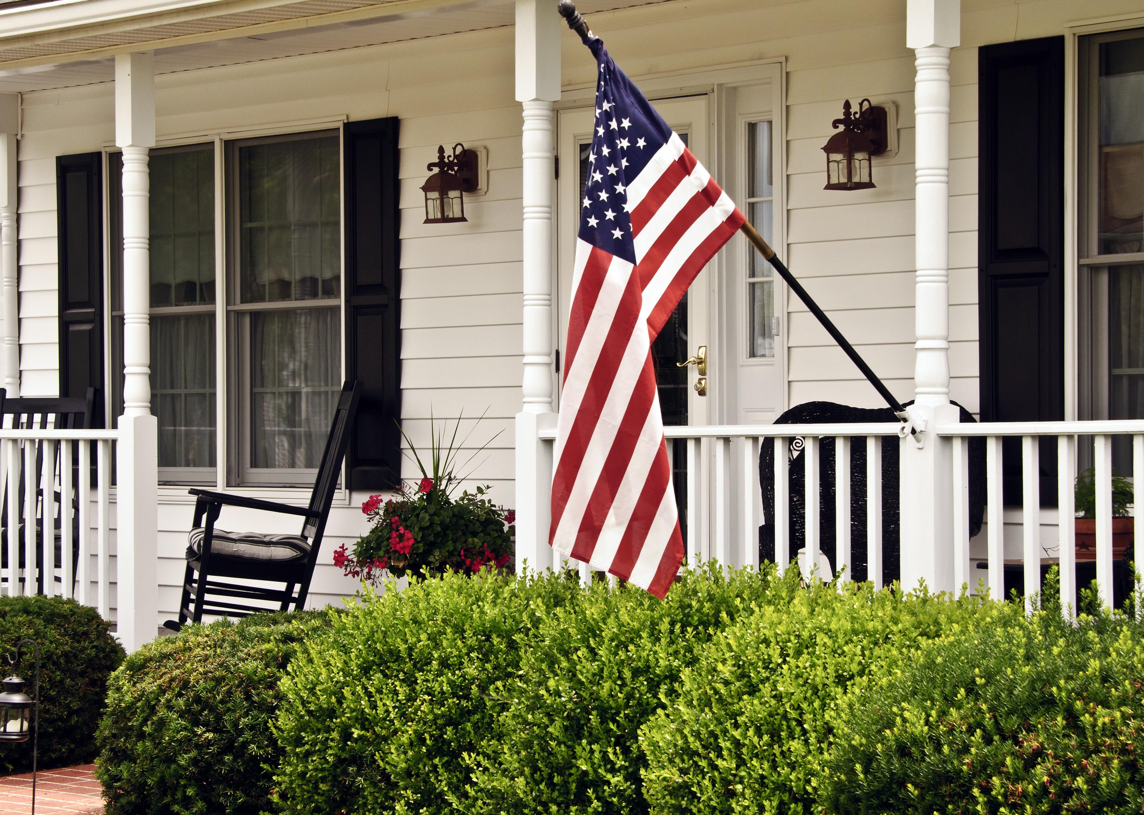 Porch of white colonial-style home with black shutters and American flag.