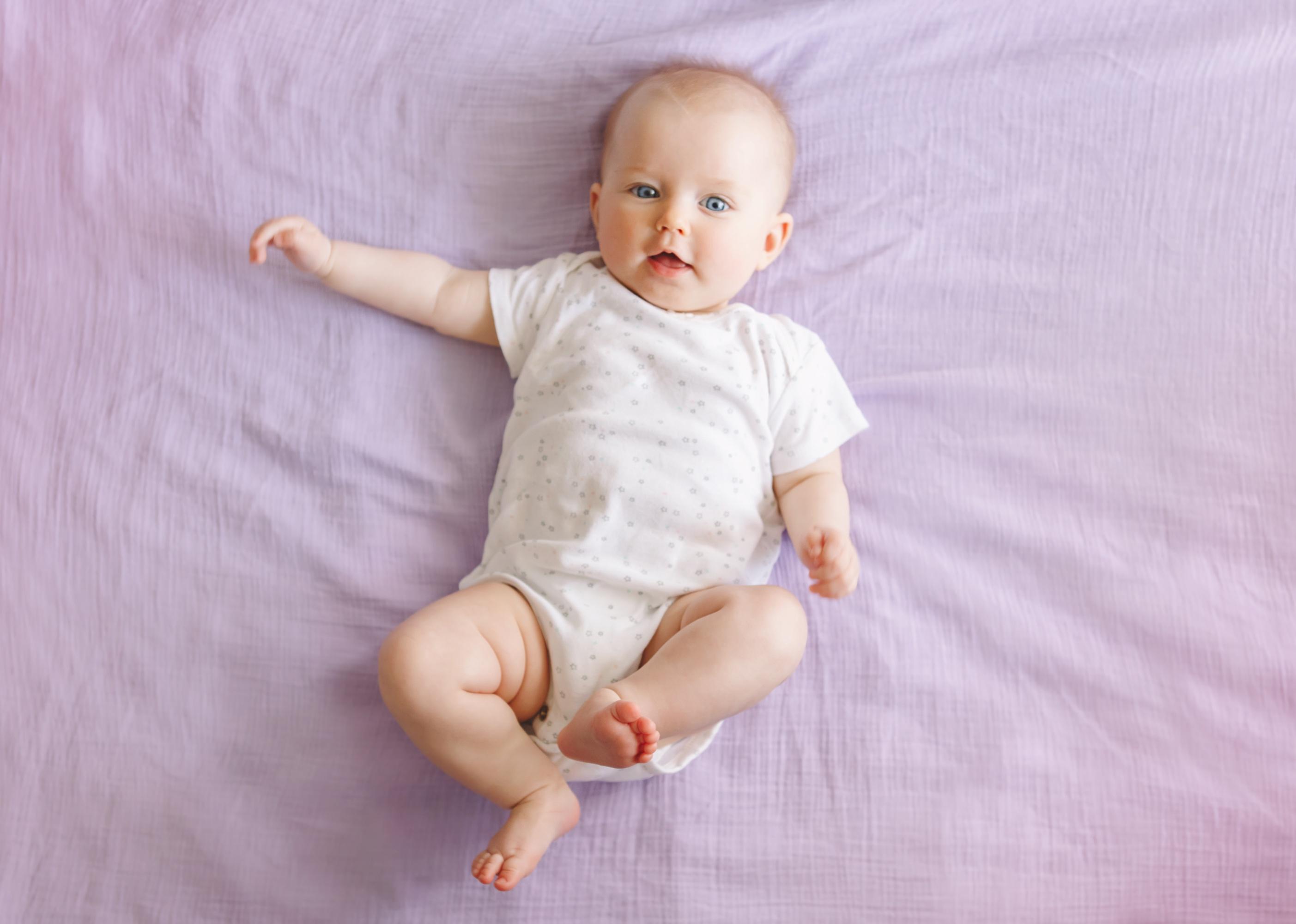 Smiling baby with blue eyes on purple bedding. 